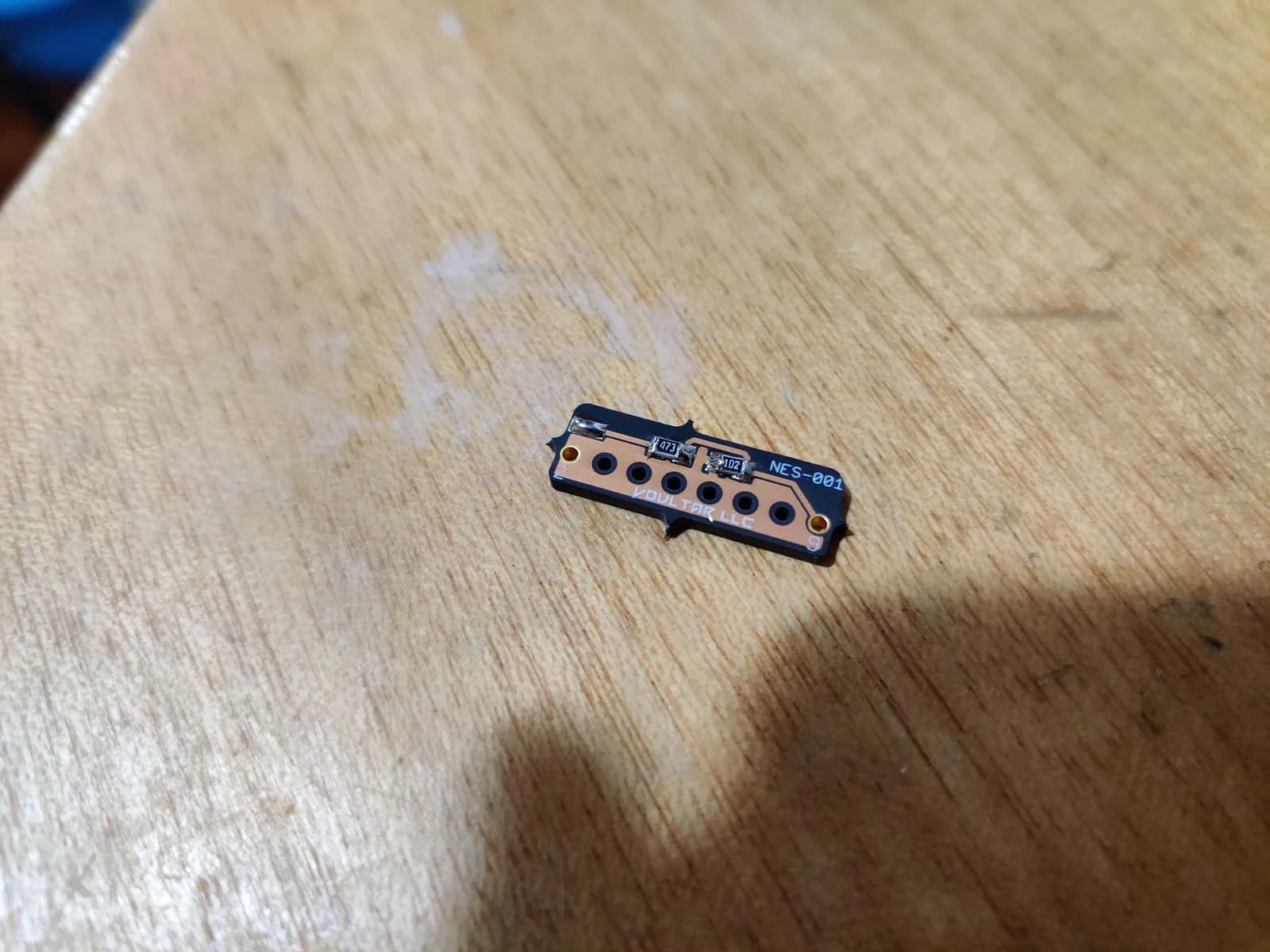 NES-001 expansion audio board with six circular component holes and black PCB mounted on wooden surface, first assembled mod.