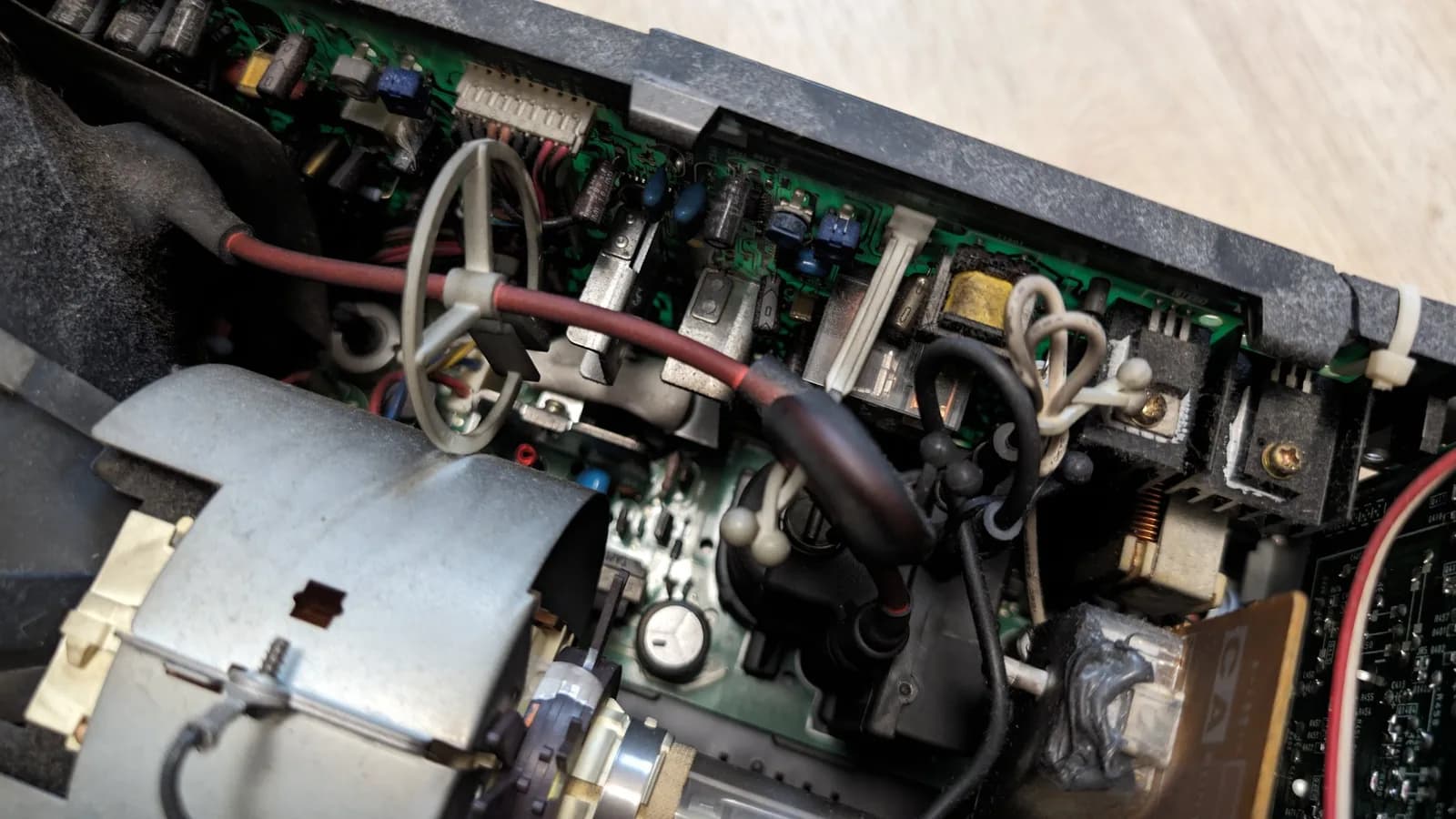Dusty interior of the Sony PVM-9045QD around the flyback and CRT neck, the red high-voltage anode lead and its rubber cap, electrolytic capacitors, and the deflection board with its transformer, plus cable-tied wiring, before cleaning.