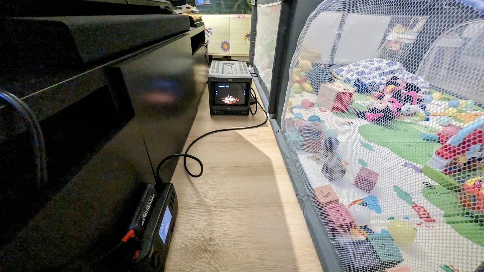 On arrival day, the little Sony PVM-9045QD on the floor playing Streets of Rage 2 from a Sega Nomad (a Mega EverDrive Pro cart in it), beside a TV stand at left and a mesh baby playpen of toys at right.