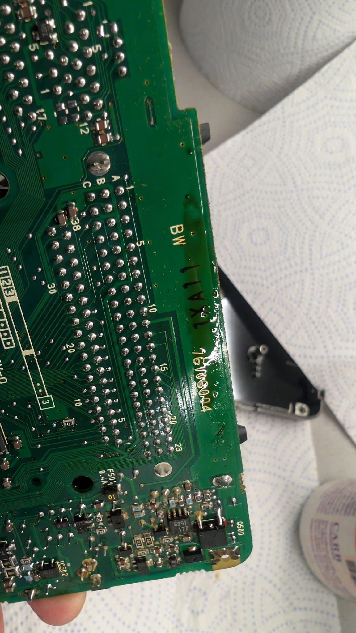 Solder side of the PC Engine LT board held in hand, showing through-hole joints and a small SMD section, with a pale smear of leaked electrolyte along one edge.