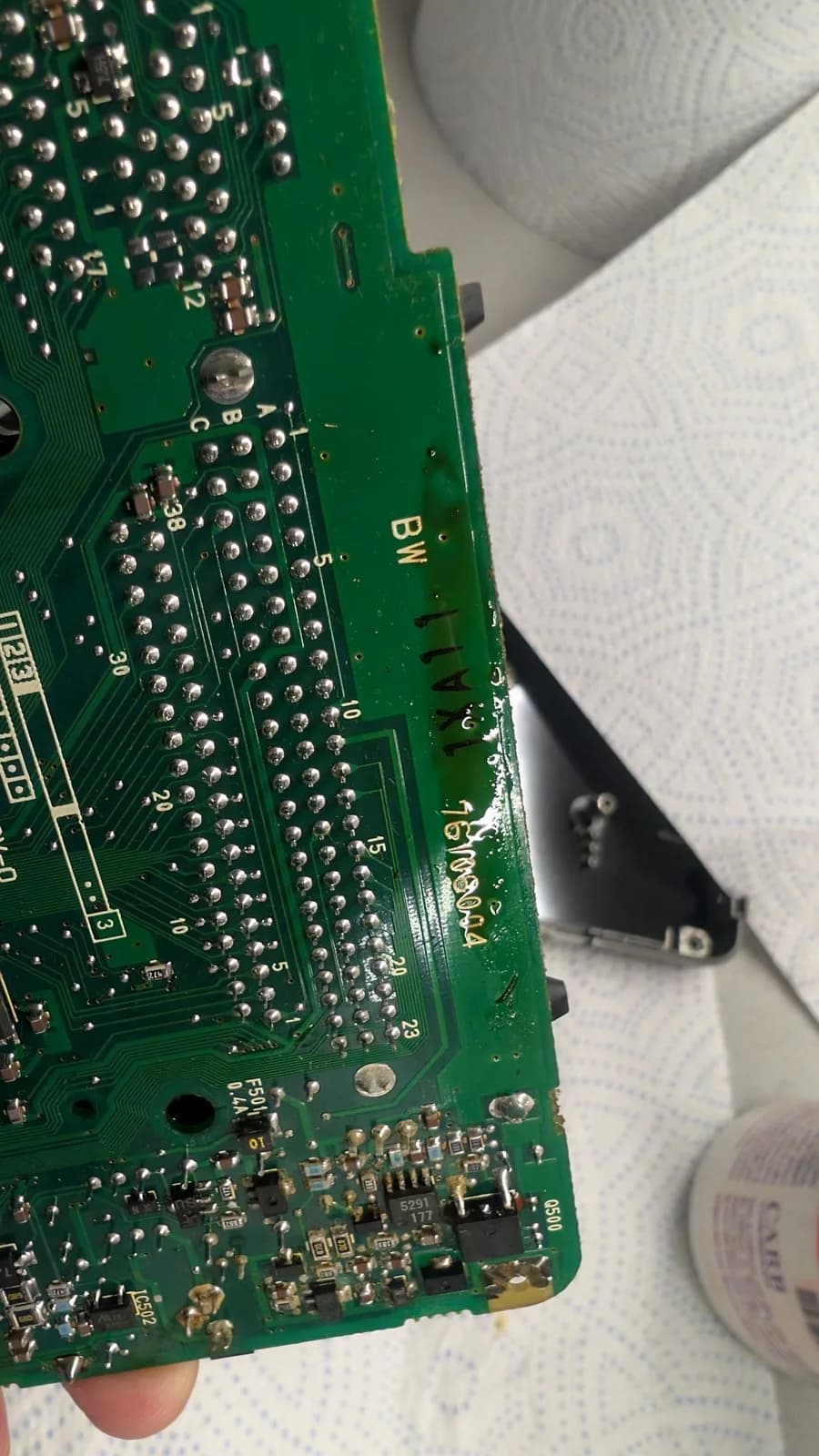 Solder side of the PC Engine LT board held in hand, showing through-hole joints and a small SMD section, with a pale smear of leaked electrolyte along one edge.