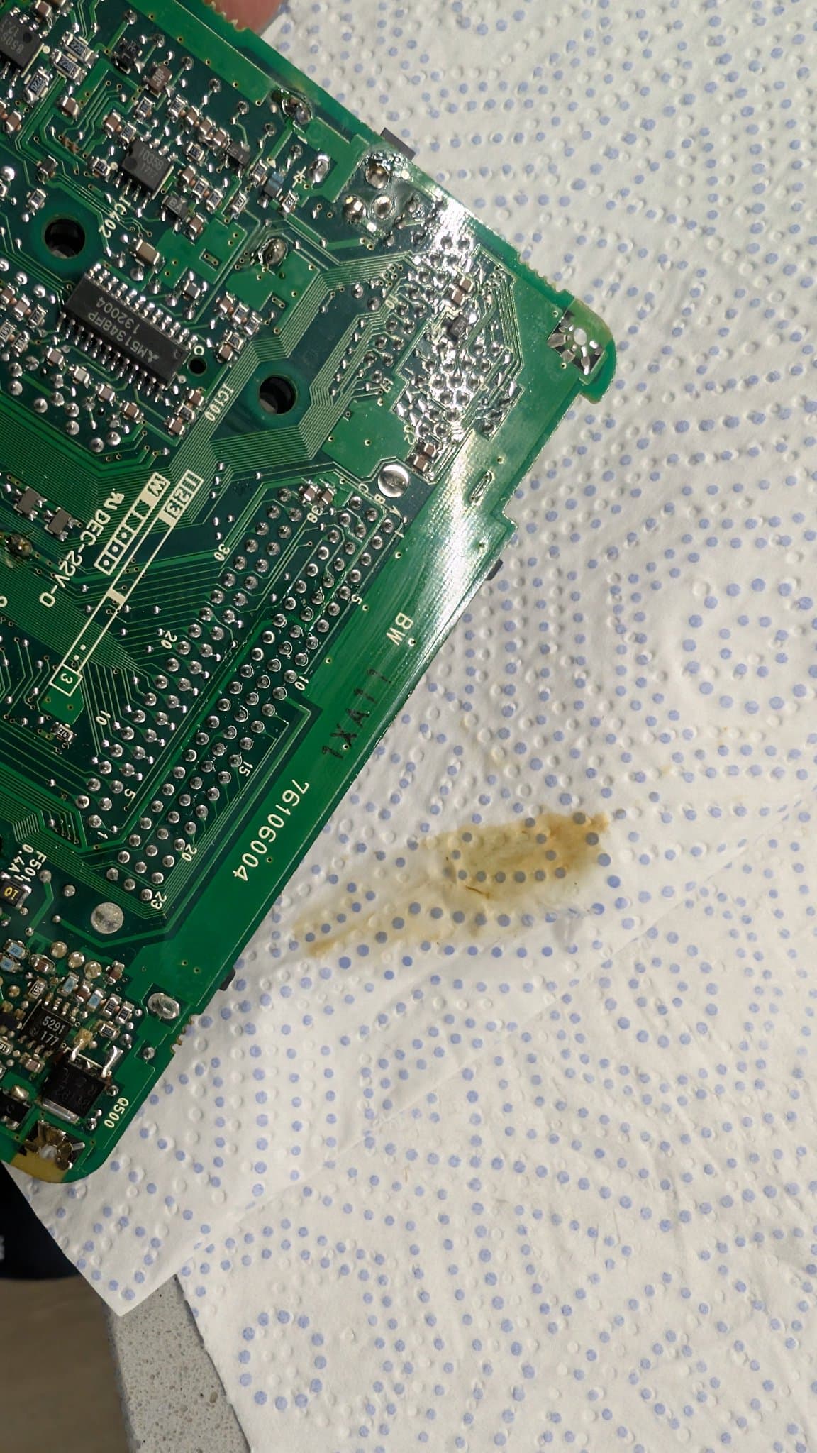 Solder-side corner of the PC Engine LT board over a paper towel, with brown electrolyte residue pooled on the tissue beside it.
