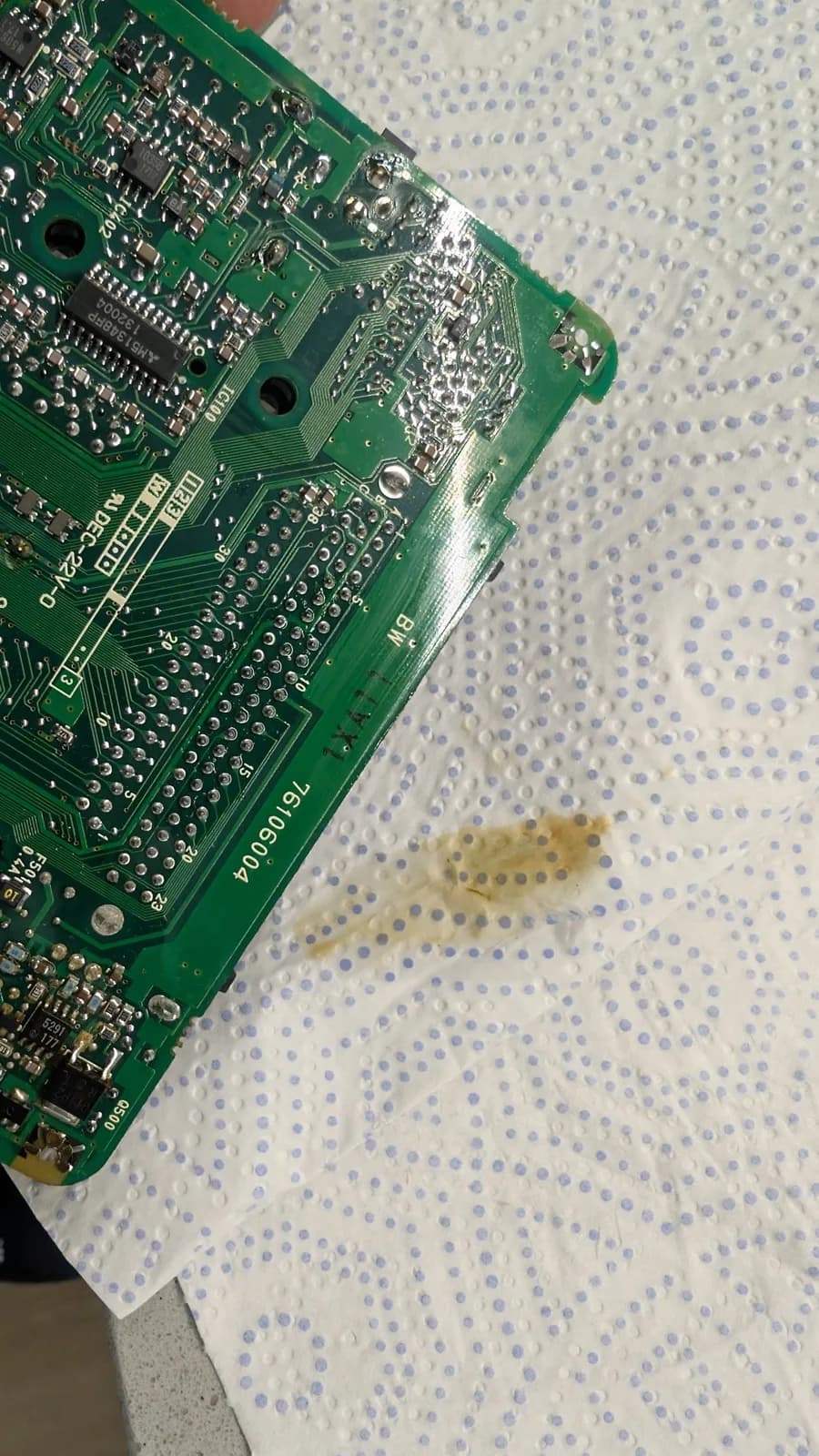 Solder-side corner of the PC Engine LT board over a paper towel, with brown electrolyte residue pooled on the tissue beside it.