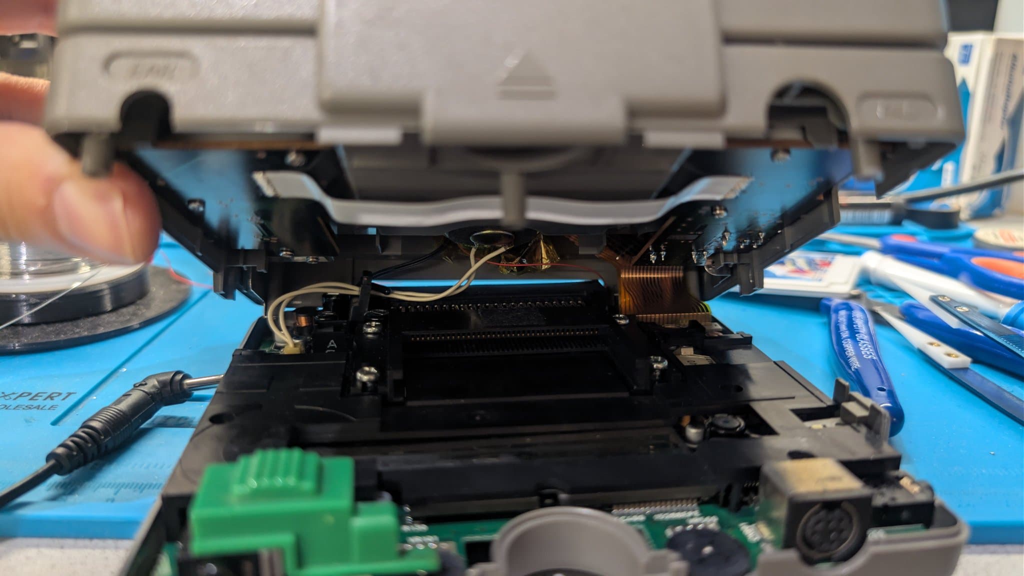 Low angle into the opened PC Engine LT showing the HuCard slot, ribbon and coil wiring, and the lower circuit board with a DIN-style connector, plus the wires running up into the boost and inverter module seated in the top-shell recess.