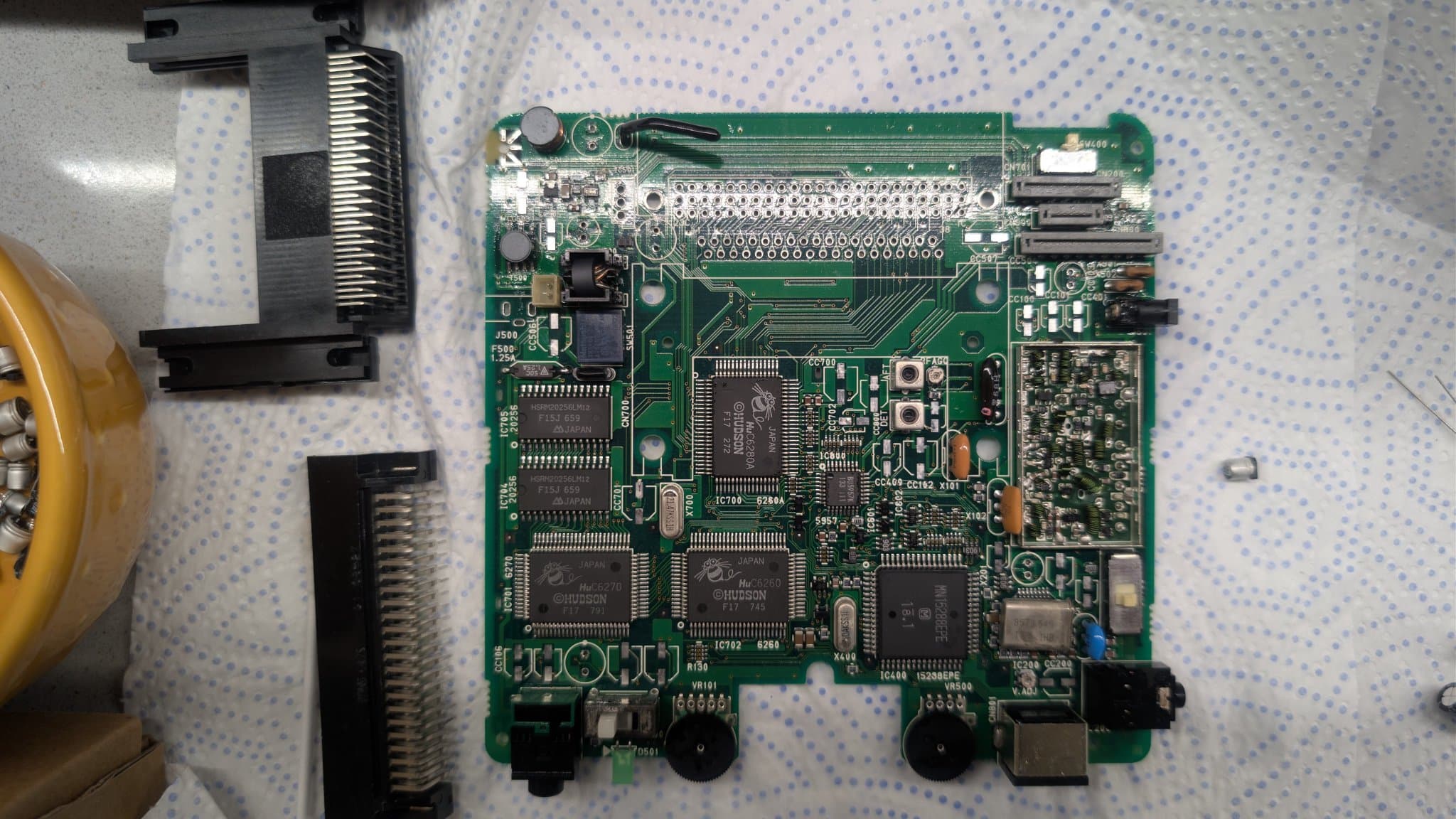 NEC PC Engine LT mainboard (component side) on a cloth after the ultrasonic bath, showing how clean the board and its two removed connectors came out with all the electrolyte gone, some of the old capacitors visible to the right of the PCB.