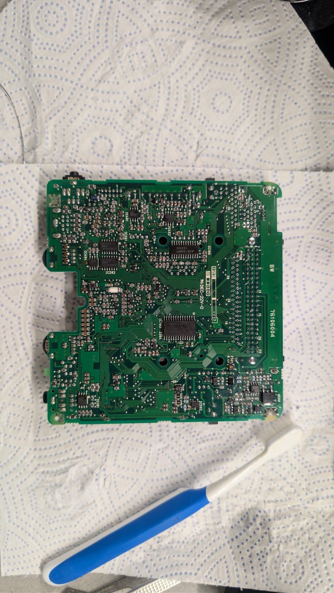 NEC PC Engine LT board (solder side) on a cloth with a blue-handled cleaning brush beside it, showing how clean it came out after the ultrasonic bath.