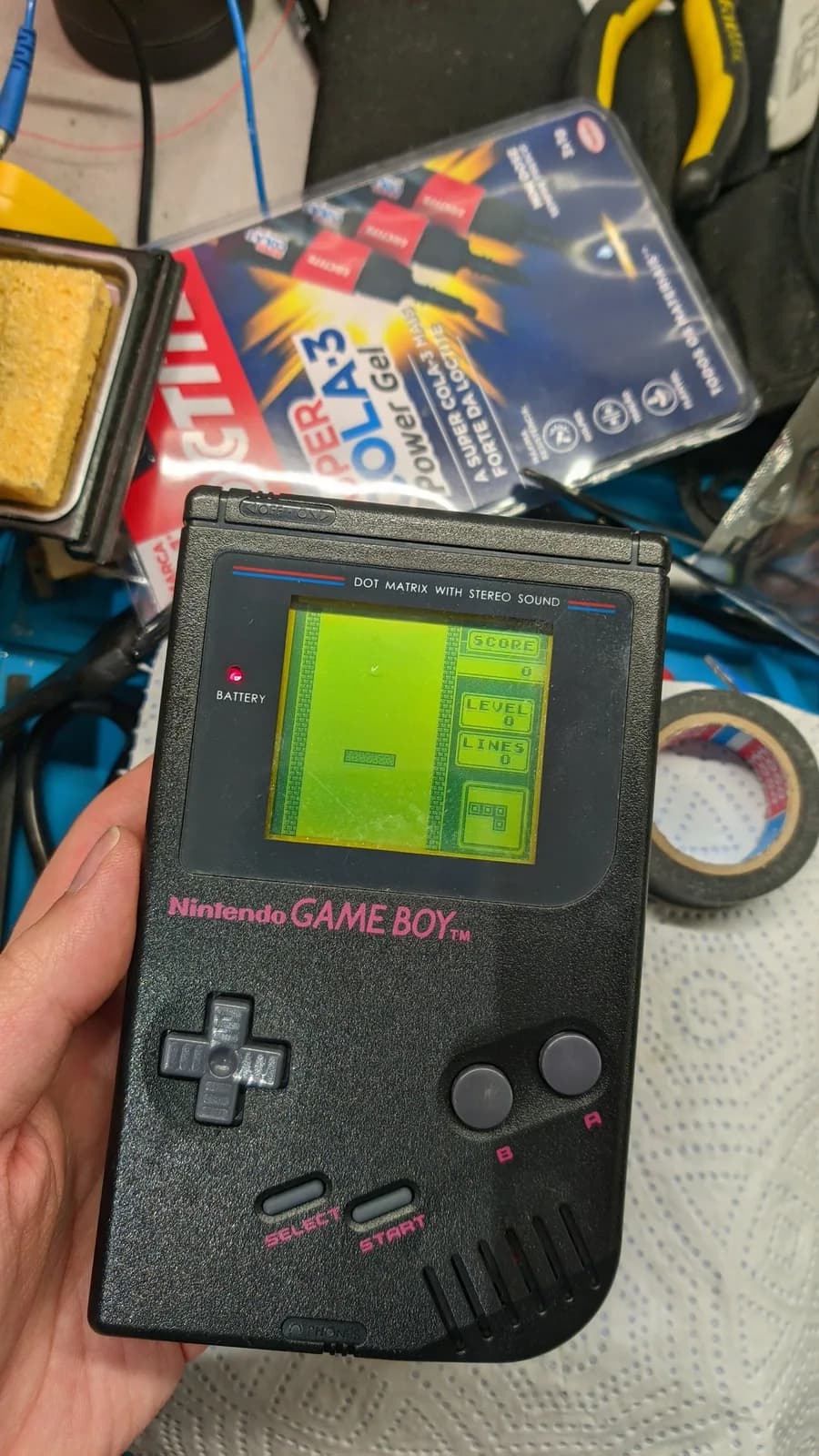The finished black Play It Loud! Game Boy held in hand, powered on and running Tetris on its restored screen.