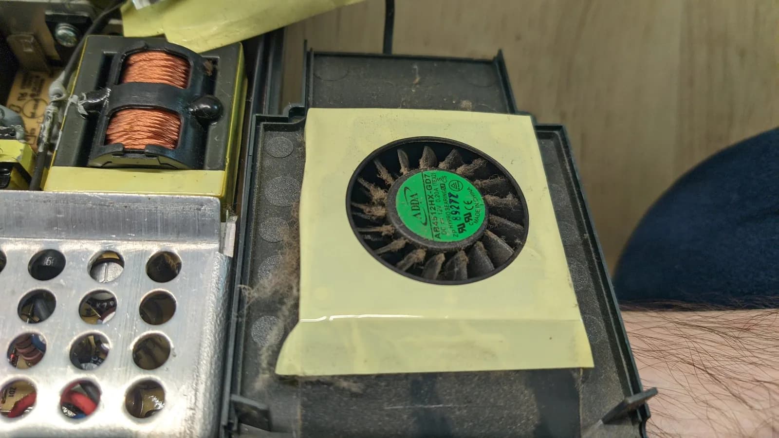 The Xbox 360 power supply (PSU) caked in dust, the transformer's copper windings and the fan visible, at the start of the teardown.