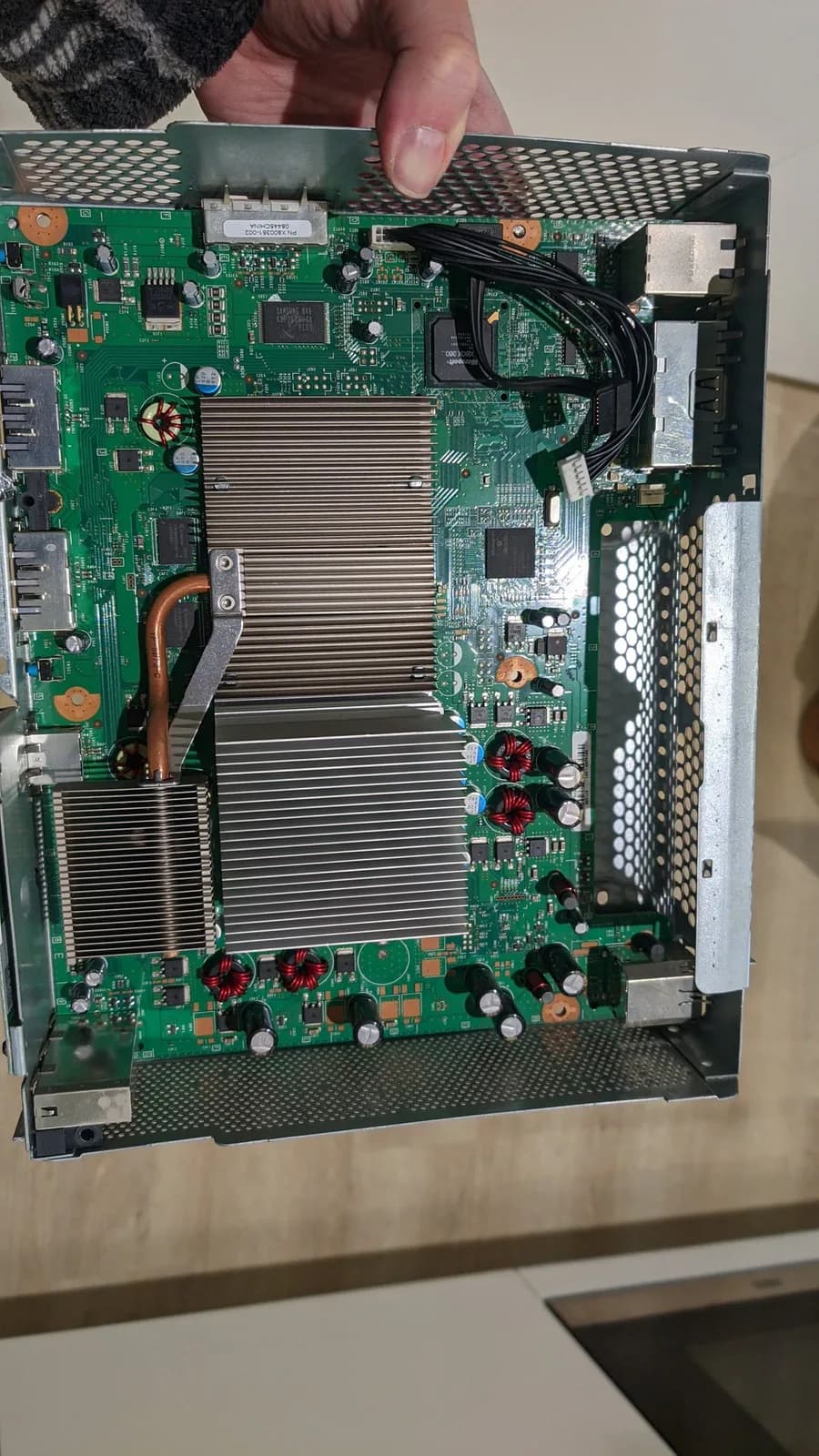 The Xbox 360 motherboard still inside its metal cage with the heatsink attached, only the fan shroud and fans removed, exposed during the teardown.