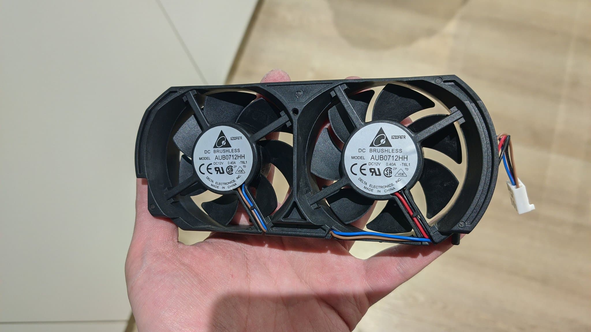 Two Delta AUB0712HH brushless cooling fans with blue and red wires held in palm, removed from Xbox 360 during laser replacement repair.