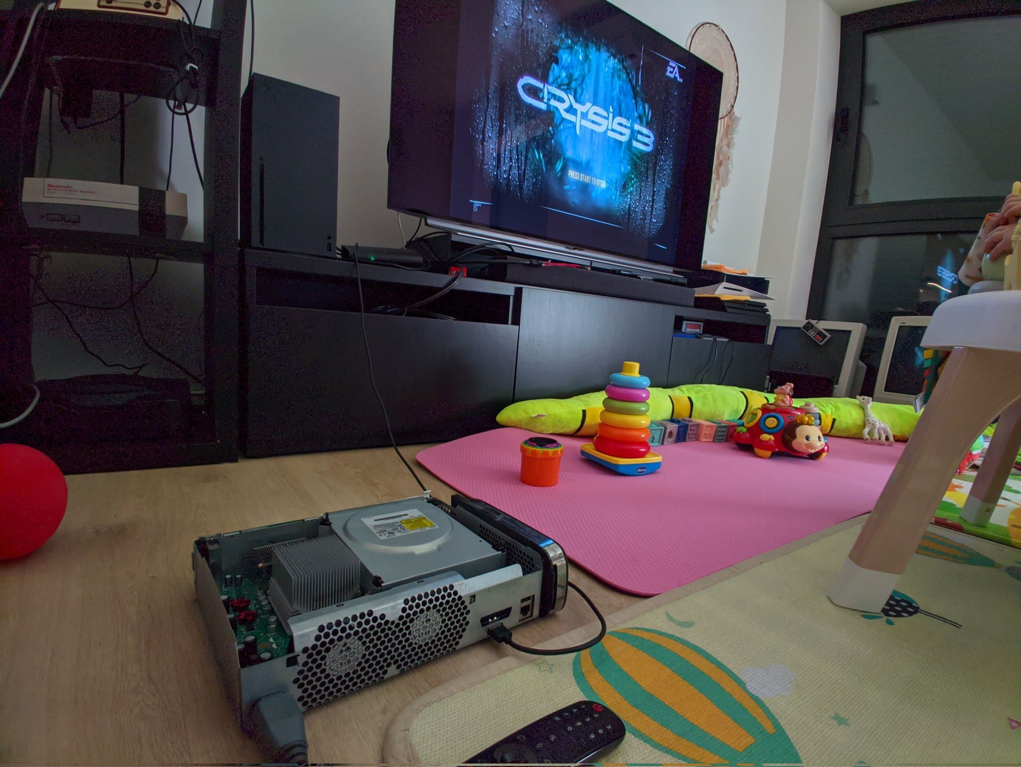 Xbox 360 console with open case displaying disc drive mechanism, laser lens visible, positioned on wooden floor next to gaming setup with pink play mat.