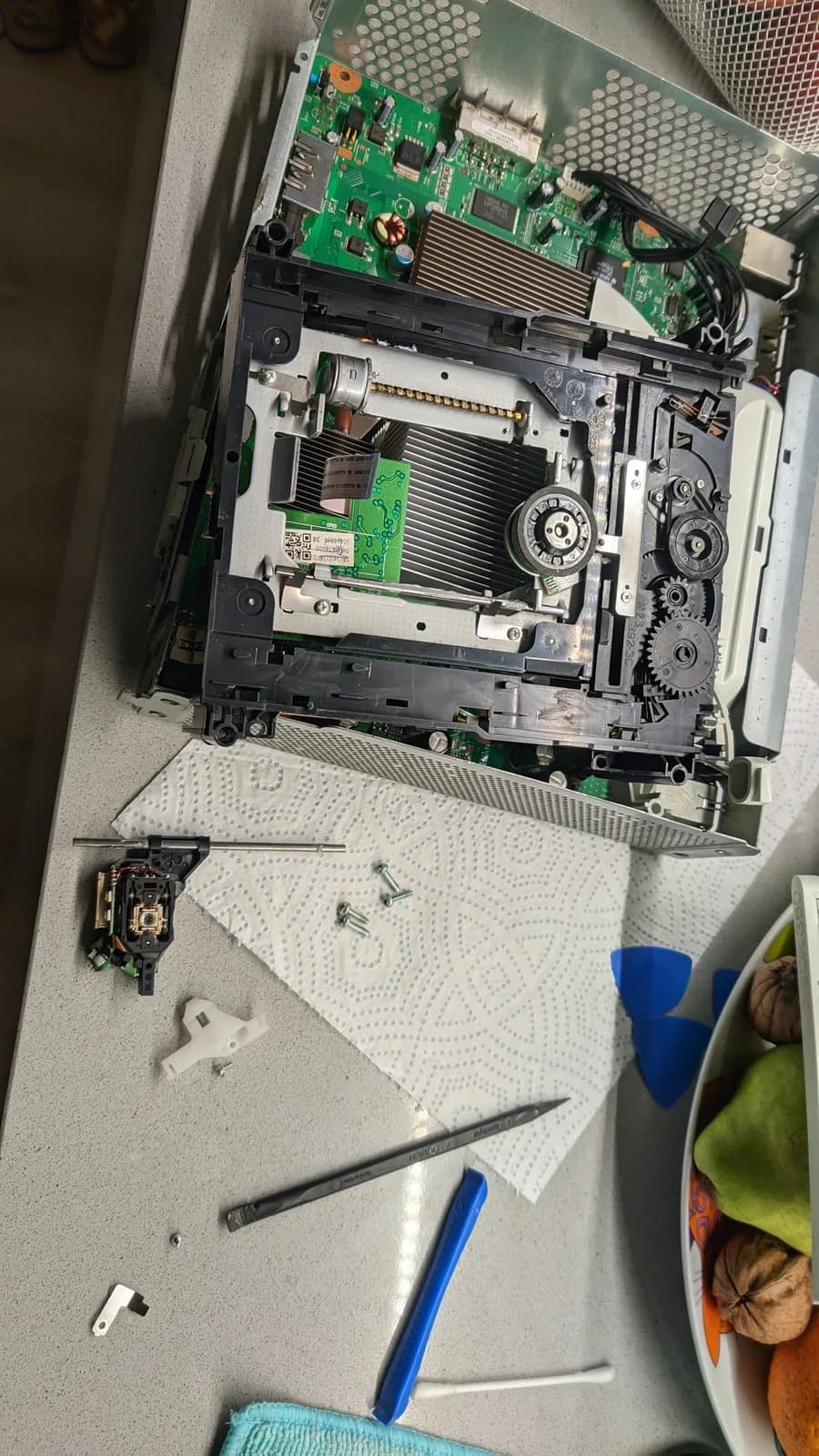 The Xbox 360 disc drive sled disassembled for the laser replacement and lubrication, the parts and tools on the bench.