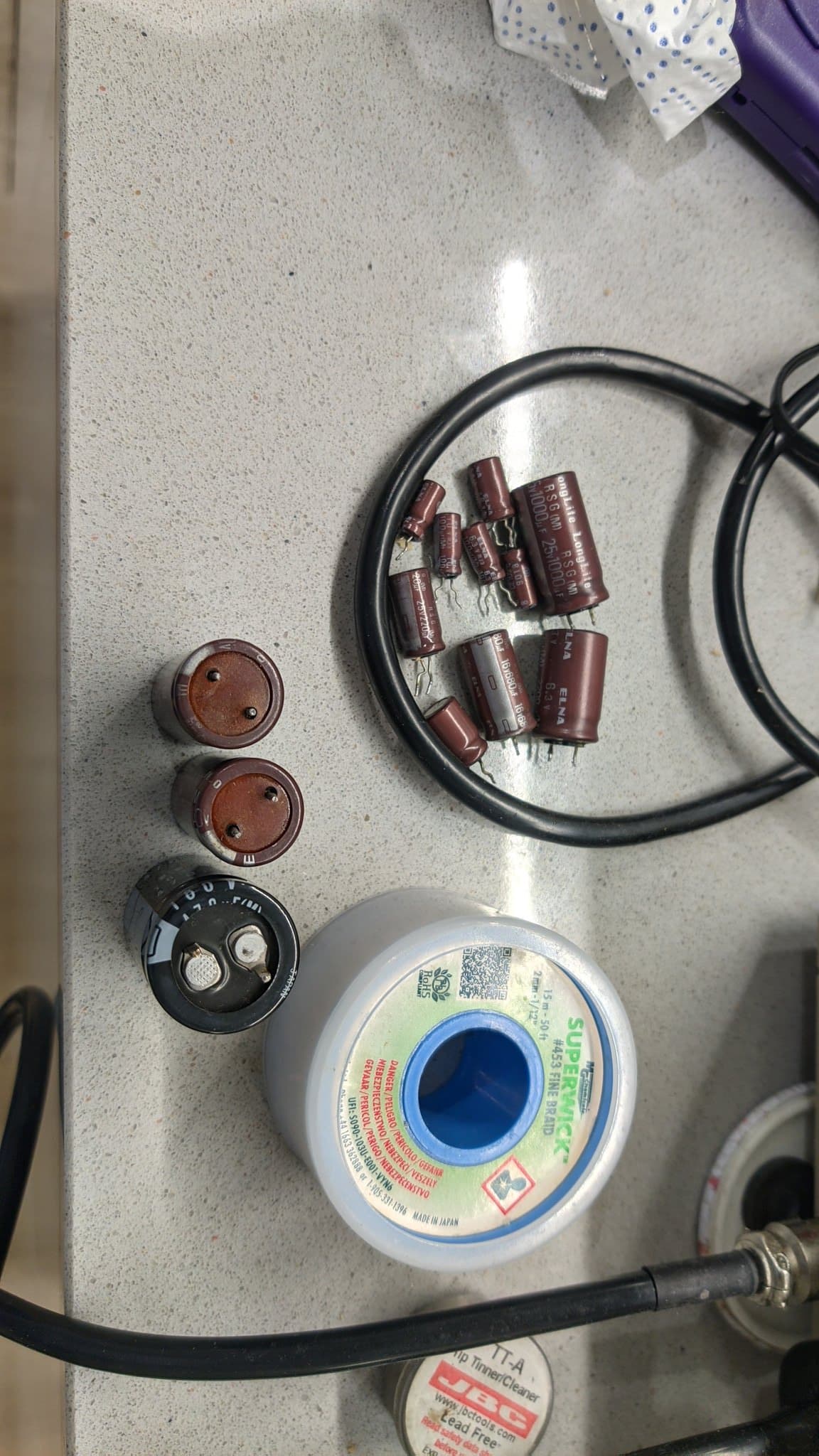 The old Elna electrolytic capacitors after extraction from the power supply, beside a spool of solder wick on the workbench.