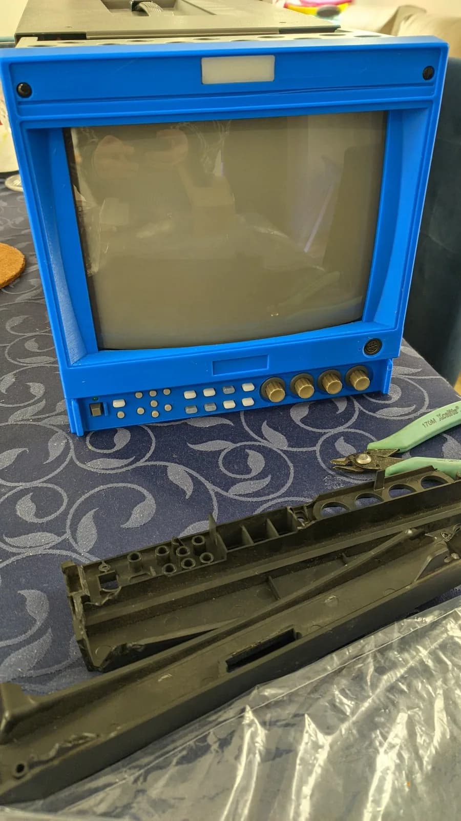 Bright blue Ikegami HTM-1005RA2 CRT monitor with disassembled bezel and internal components displayed below, alongside repair tools.