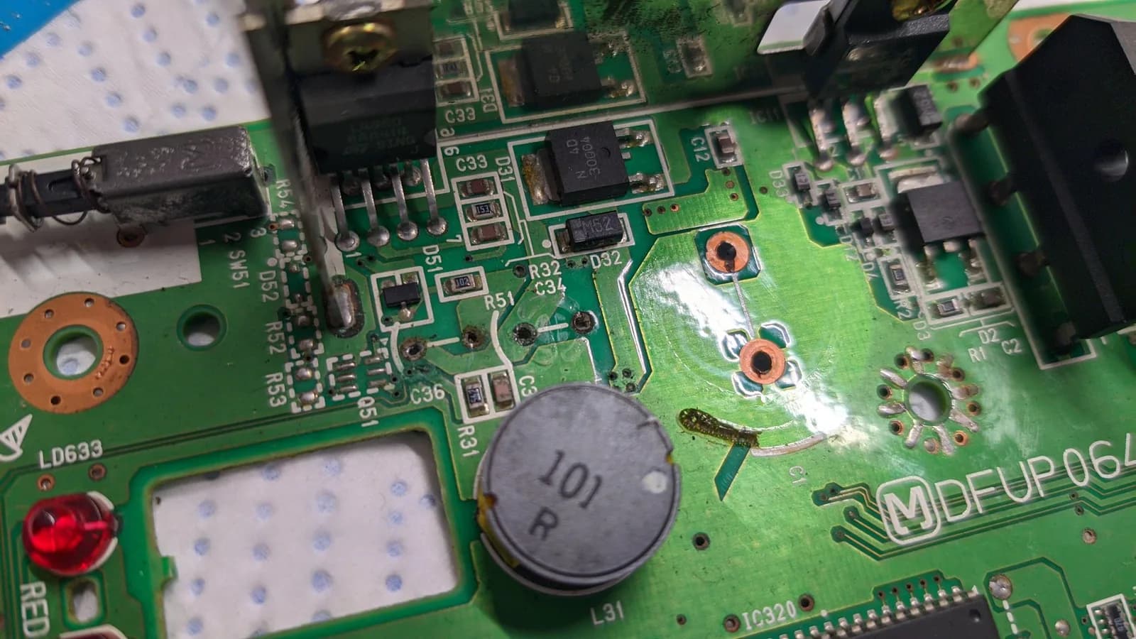 Macro of the Panasonic FZ-1 mainboard's power-supply section, the area worst hit by capacitor leakage: an L4960 regulator, the silver inductor L31 (marked 101), surrounding SMD diodes and resistors, a red status LED and the Panasonic "MDFUP064" silkscreen, with the through-holes darkened and corroded from electrolyte damage.