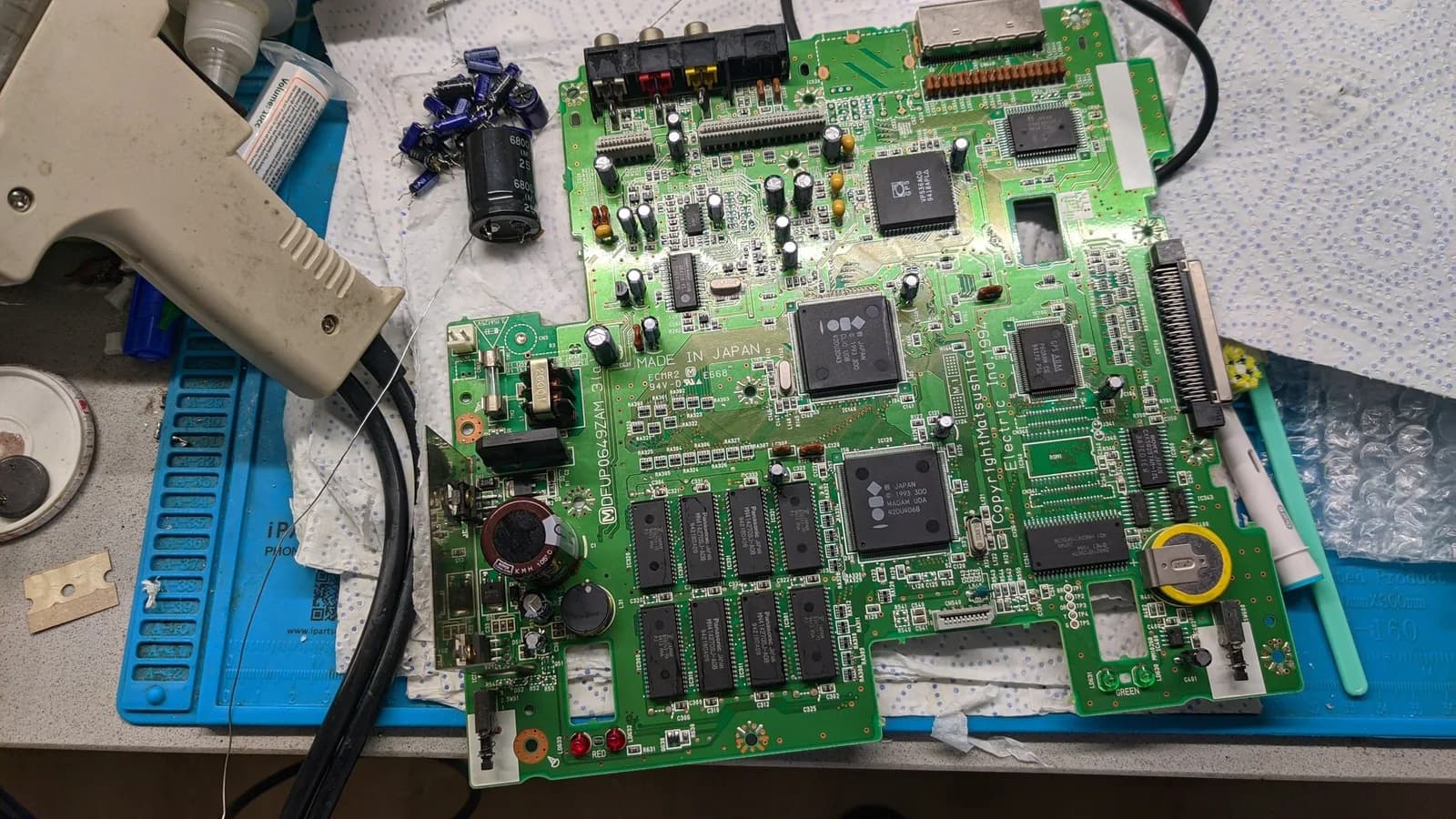 The fully recapped Panasonic FZ-1 mainboard ("MADE IN JAPAN", 3DO and MADAM chips visible), the removed old capacitors piled beside it (including a large 6800uF), with a desoldering gun and brush nearby.