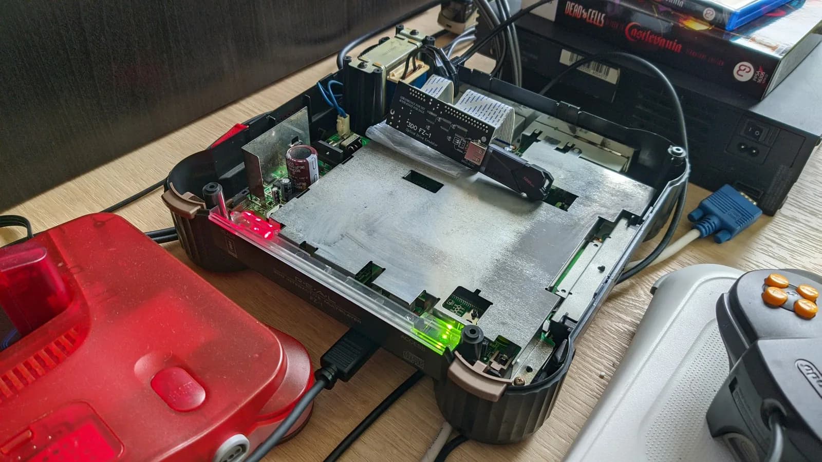 The opened Panasonic FZ-1 3DO powered on, its red READY and green ACCESS LEDs lit and fresh electrolytic capacitors (a 6800uF among them) visible; the black 3DO FZ-1 ODE board is installed at the top-right via a ribbon cable with a SanDisk USB flash drive plugged in. A translucent red Nintendo 64 sits alongside.
