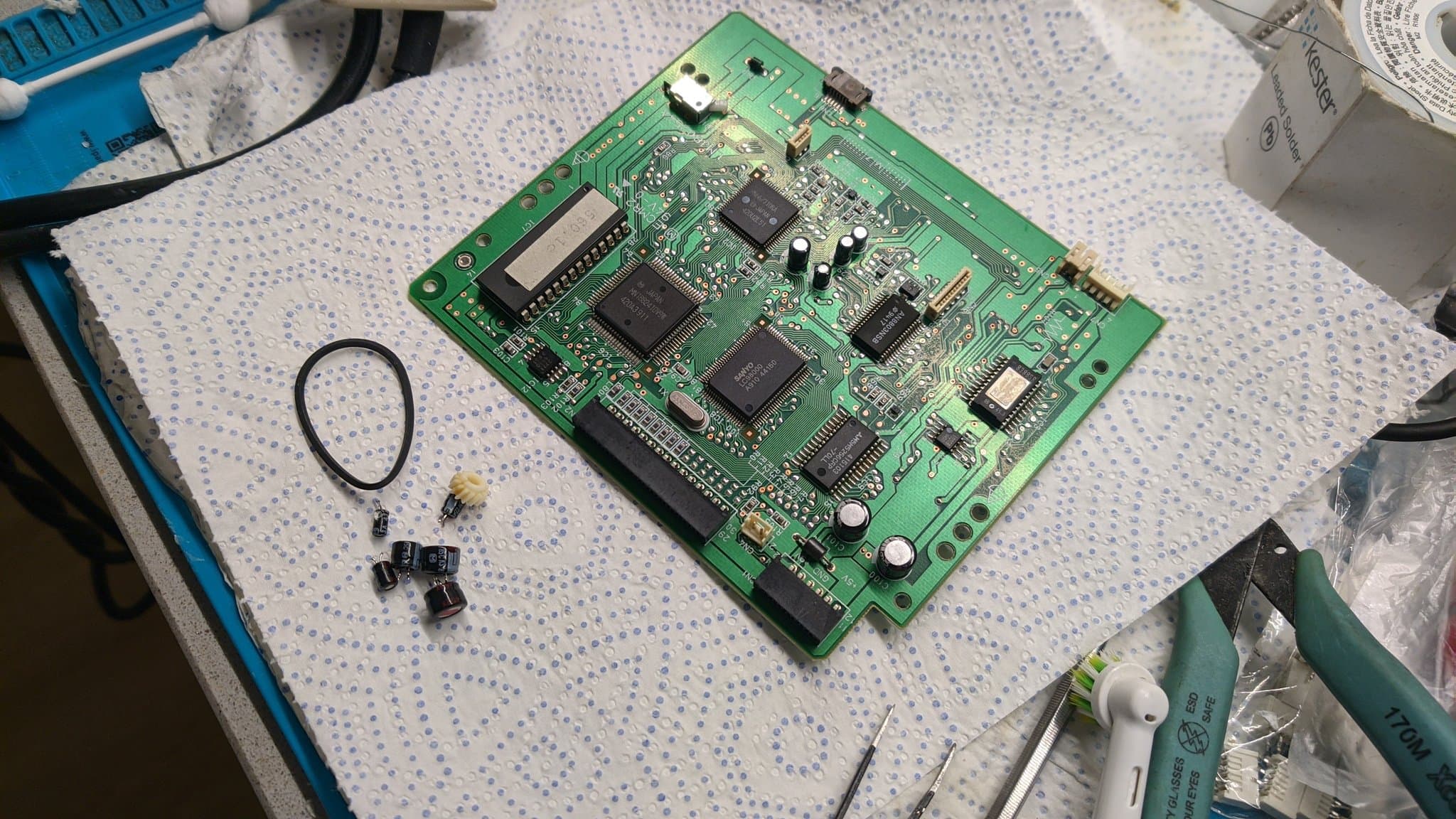 Recapped 3DO Panasonic FZ-1 disc drive PCB during restoration; desoldered ICs and capacitors visible on work surface with tools.
