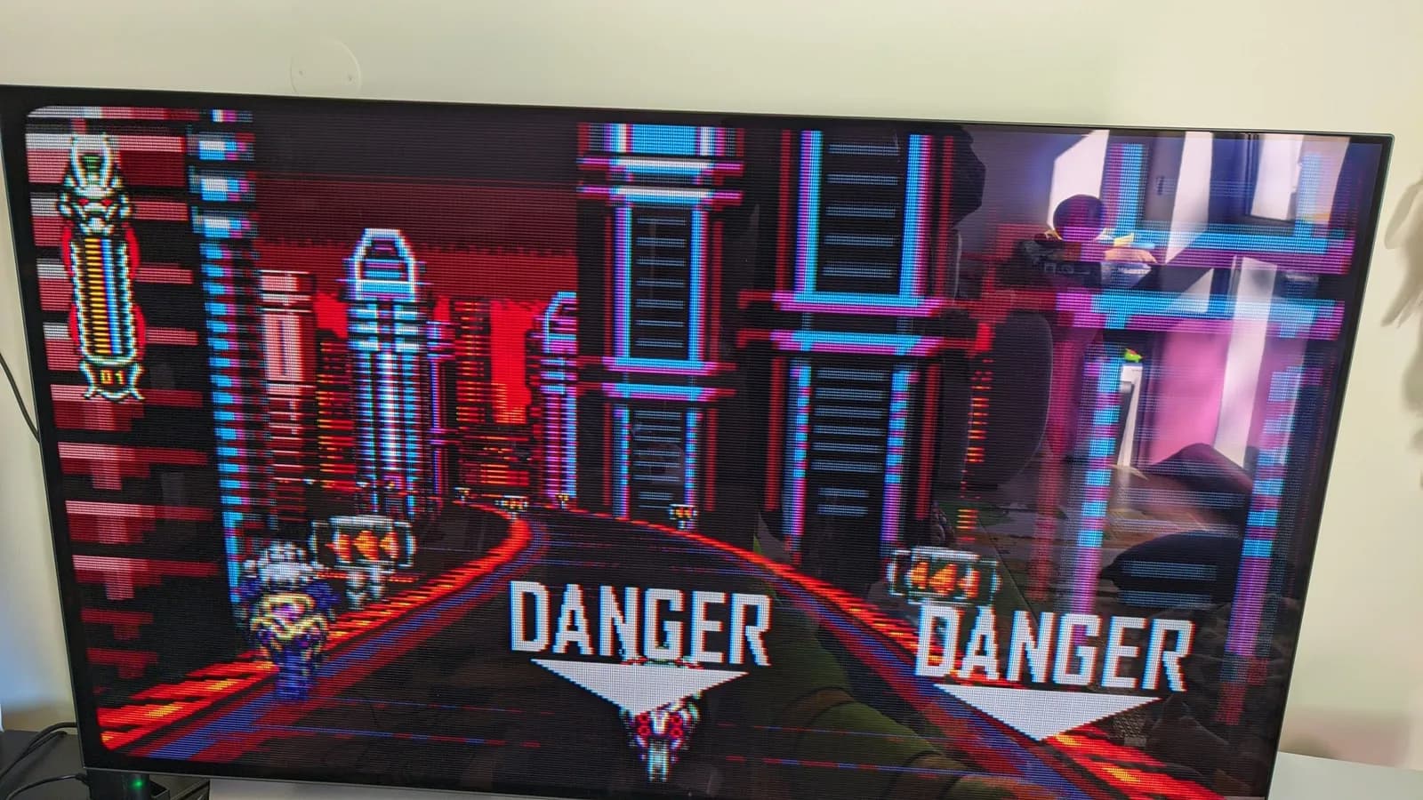Vengeful Guardian: Moonrider on a large LG C1 OLED TV, a neon cyberpunk cityscape in red and cyan with two 'DANGER' warnings and downward arrows above the player's motorcycle.