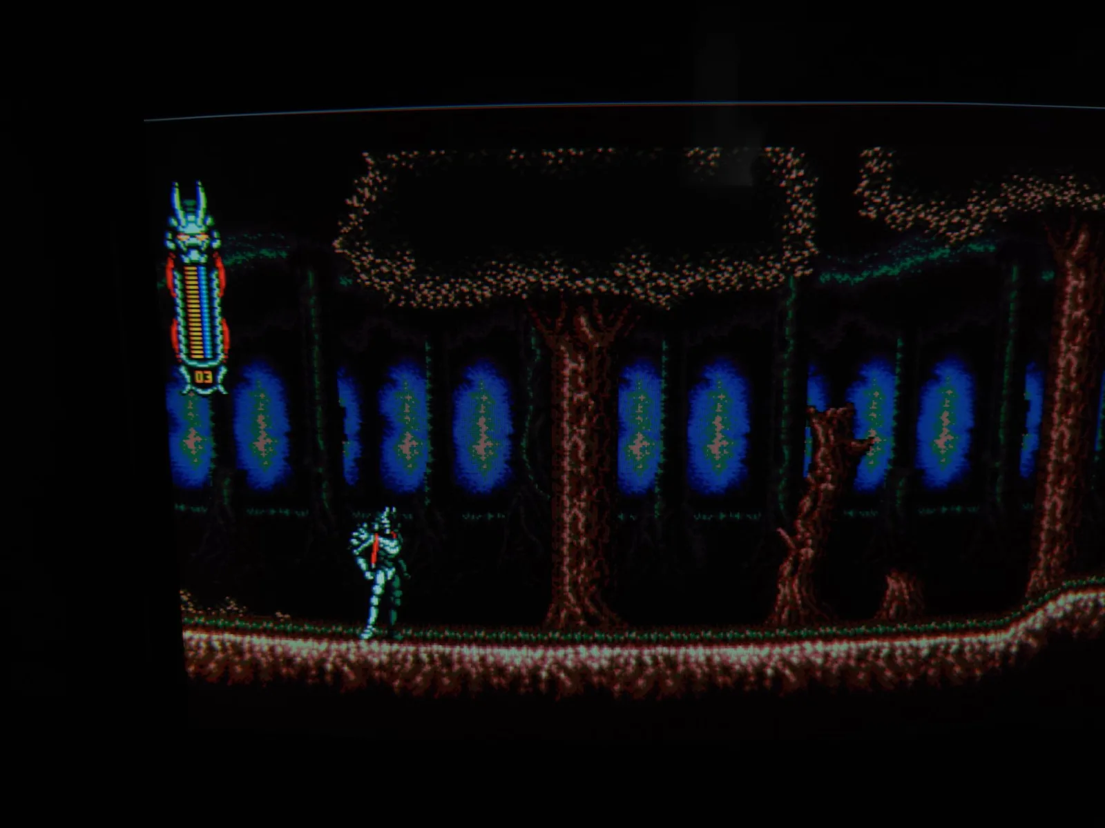 Vengeful Guardian: Moonrider on the Sony BVM-D14H1E, the armored Moonrider standing in a dark forest stage with blue glowing patches, the game's energy bar and 03 lives counter at top-left, CRT scanlines visible.