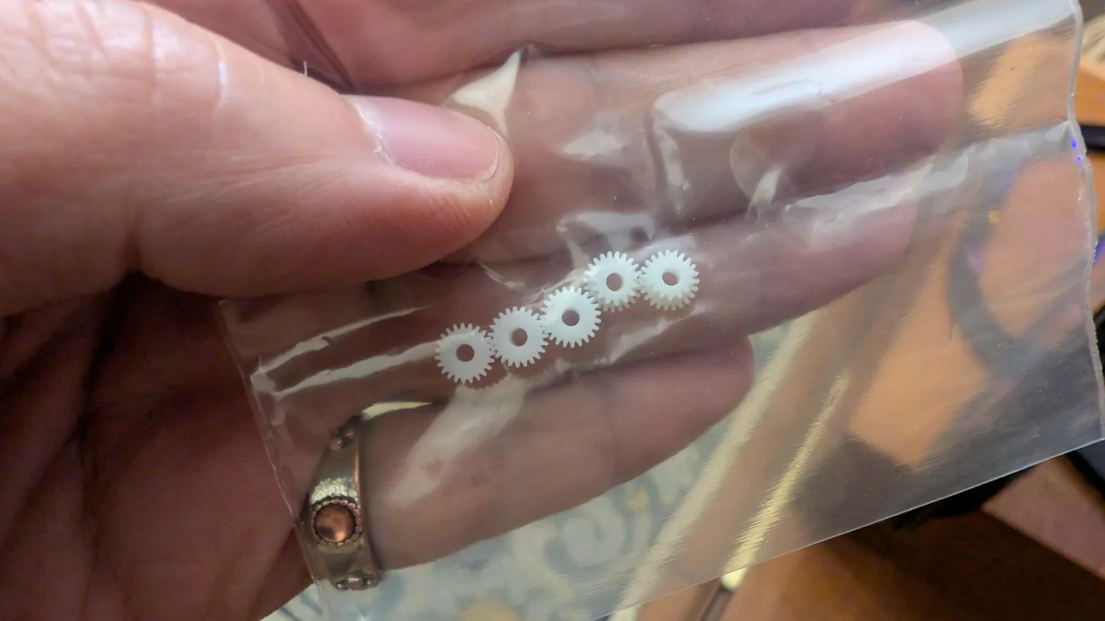 Close-up of five 3D-printed plastic gears arranged in a row on clear plastic, held by a hand during PC Engine CD-ROM2 restoration.