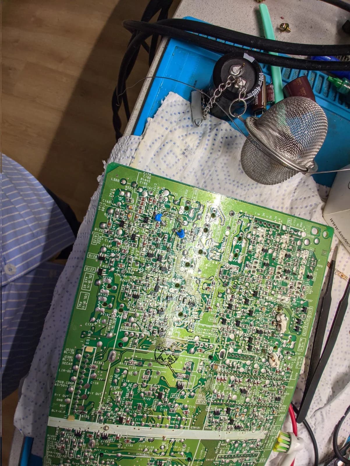 Sony PVM-9041Q B board seen from the underside on the bench, showing the ceramic capacitors added as part of the fix after the colour trimmer pots were replaced; a filter capacitor sits on the bench nearby but is not from this board.