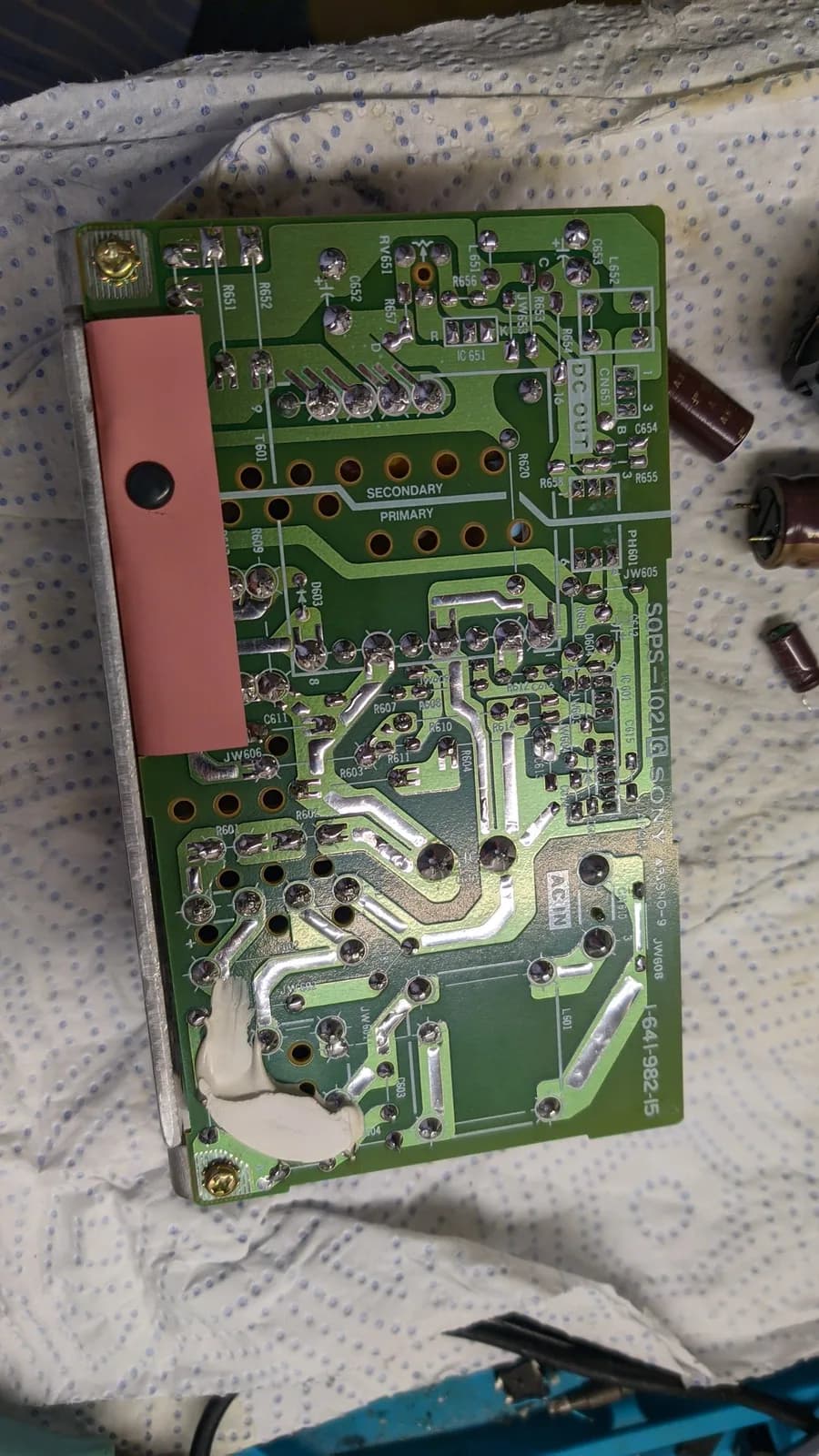 Sony PVM-9041Q PSU board solder side after recapping, the SECONDARY silkscreen and a pink insulator over the primary side, fresh shiny solder joints.