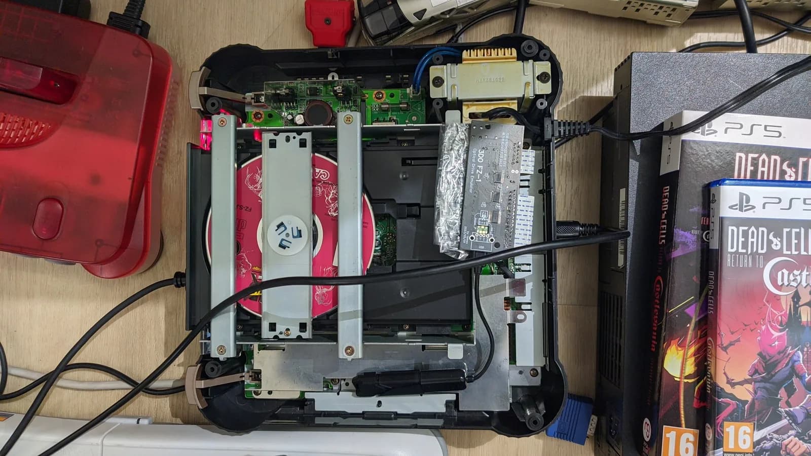 Top-down view of an opened Panasonic FZ-1 3DO on the floor, its disc-drive area exposed, the assembled ODE board connected to the ribbon cables that normally link the optical drive to the mainboard.