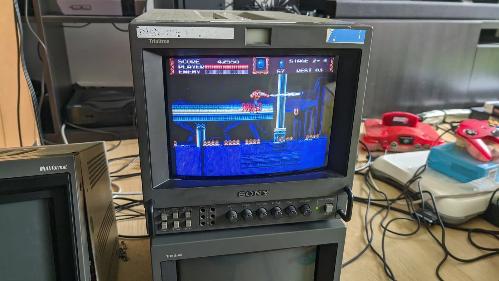 Sony PVM-9041Q stacked on top of another Trinitron (not the Multiformat), with a Sony Multiformat monitor off to the side, running Castlevania Bloodlines during the incoming test, Nintendo 64s and other consoles on the bench at right.