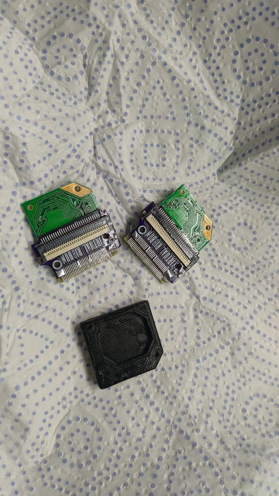 Two green circuit boards with ribbon connectors and a black mounting jig displayed on dotted fabric, showing Virtual Boy 4.0 LED array PCB assembly components.