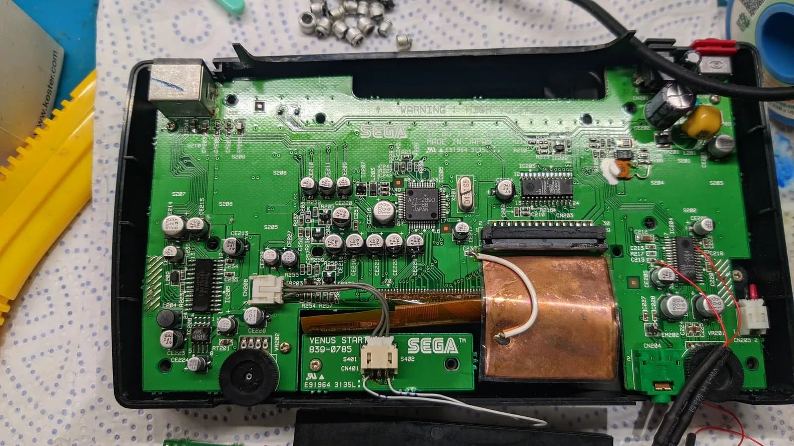 Sega Nomad motherboard with replaced electrolytic capacitors, showing green PCB, copper inductor, and IC chips during restoration work.