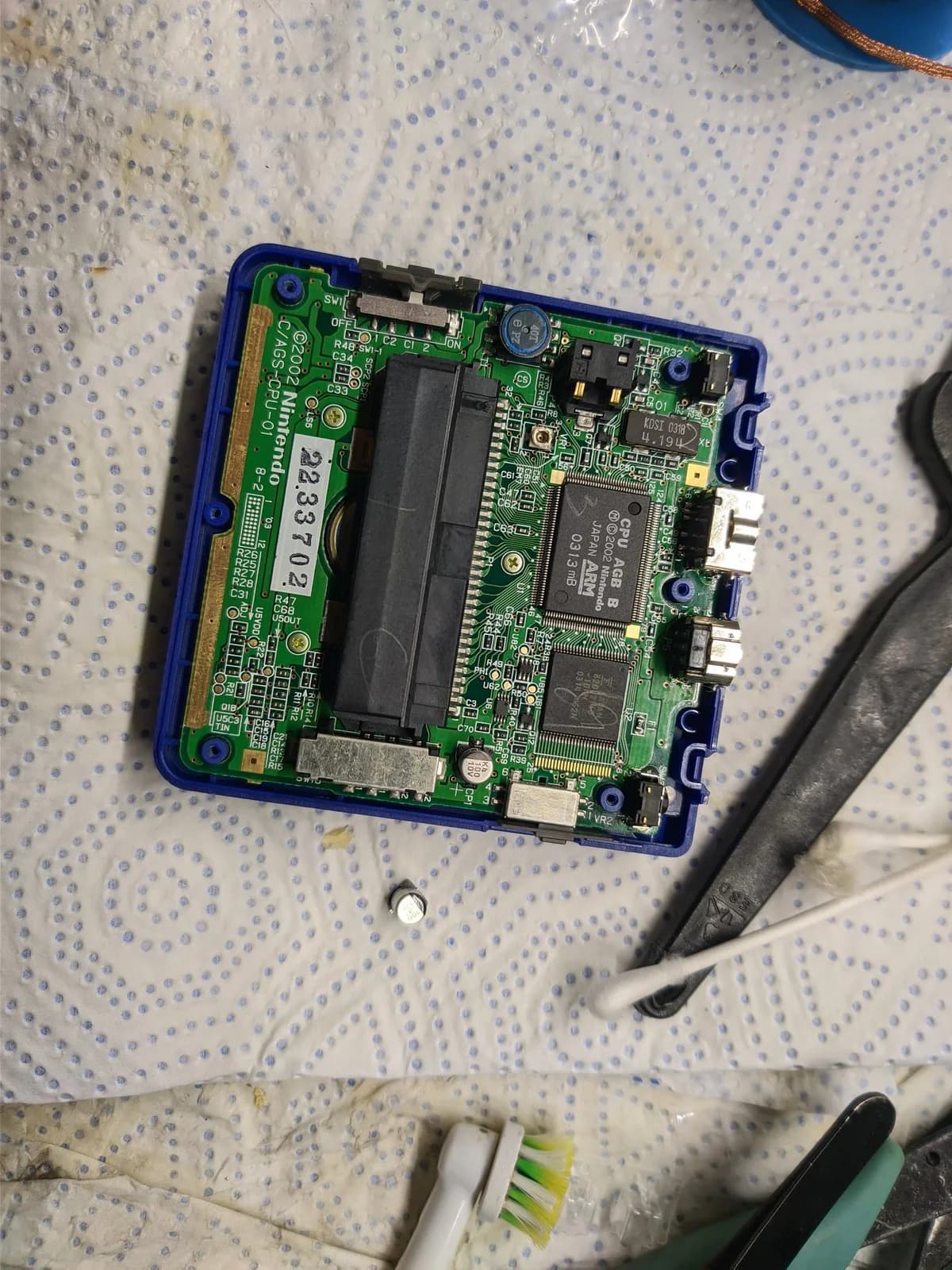 GBA SP motherboard with blue plastic housing, showing single electrolytic capacitor replacement and surrounding circuitry on green PCB.
