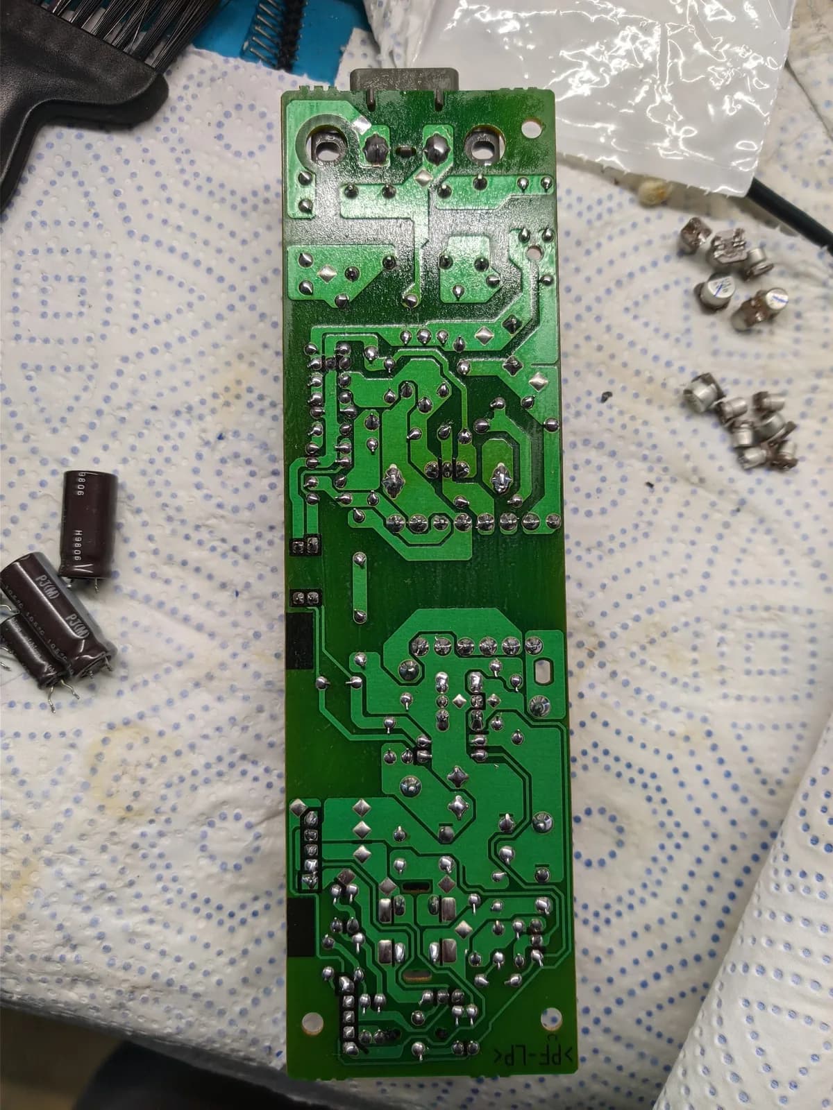 Sony PS1 PSU board during recap; electrolytic capacitors and components removed, cracked solder joints visible on power jack area.