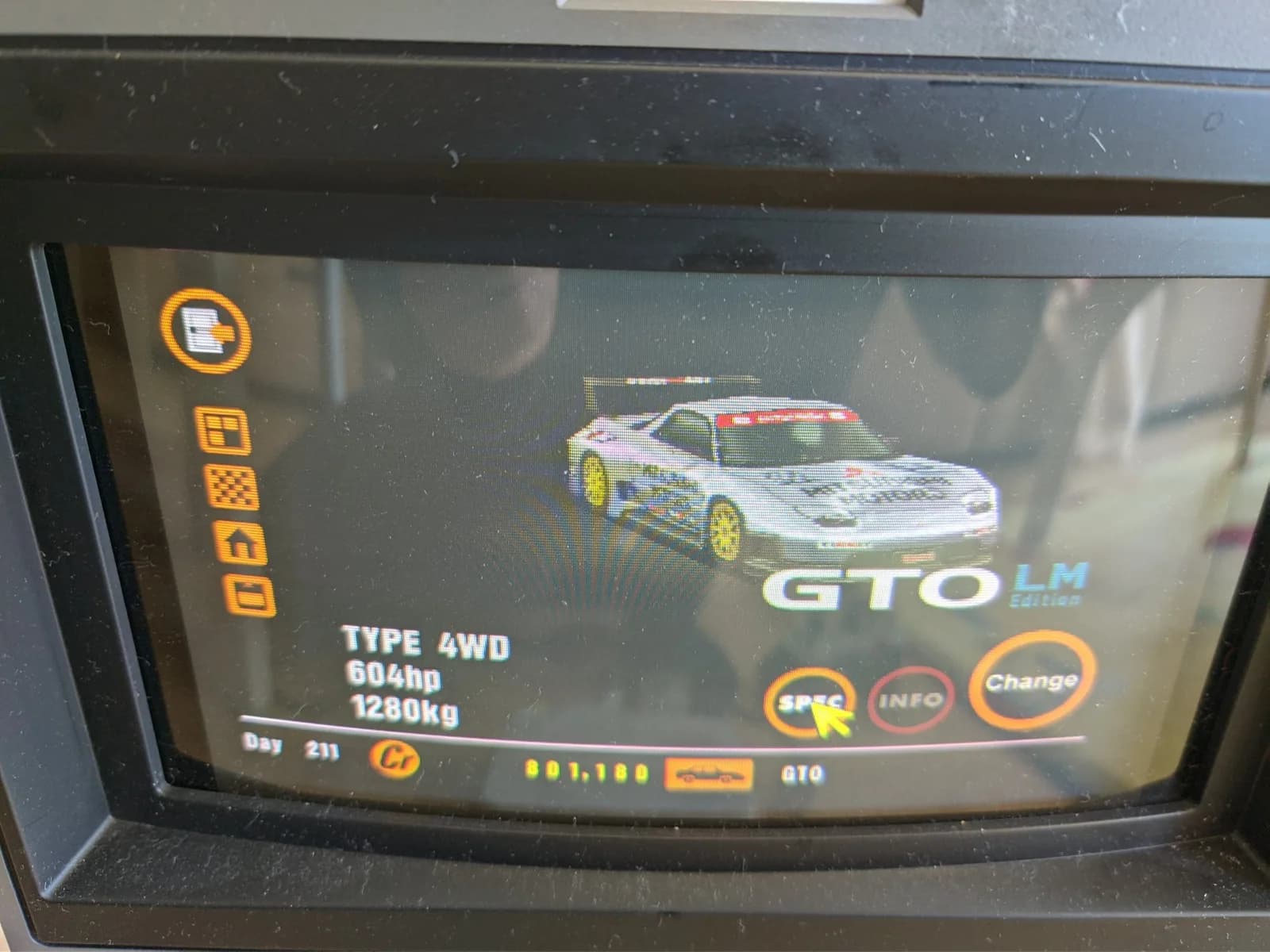 Close-up of a CRT showing the Gran Turismo garage screen for the silver Mitsubishi GTO LM Edition, a race car with a large rear wing, listing TYPE 4WD, 604hp and 1280kg with SPEC, INFO and Change options.