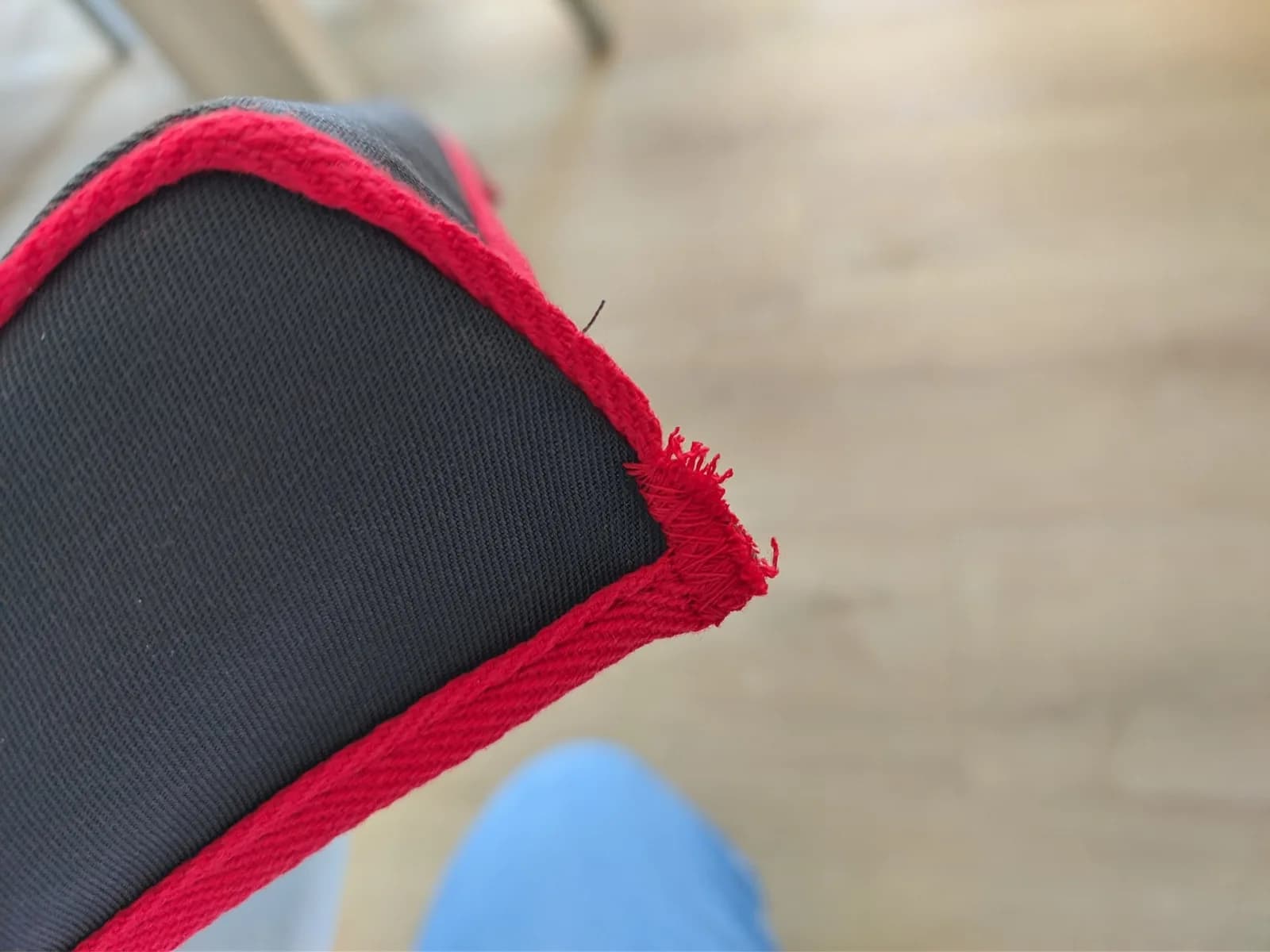 Close-up of frayed red trim edge on black dust cover, showing poor finishing quality on protective case.