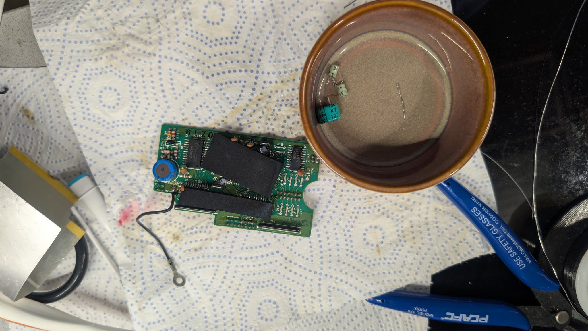 The NEC IFU-30 daughterboard that carries the save-data supercapacitor, now recapped, with the old capacitors and the old supercapacitor in a bowl.