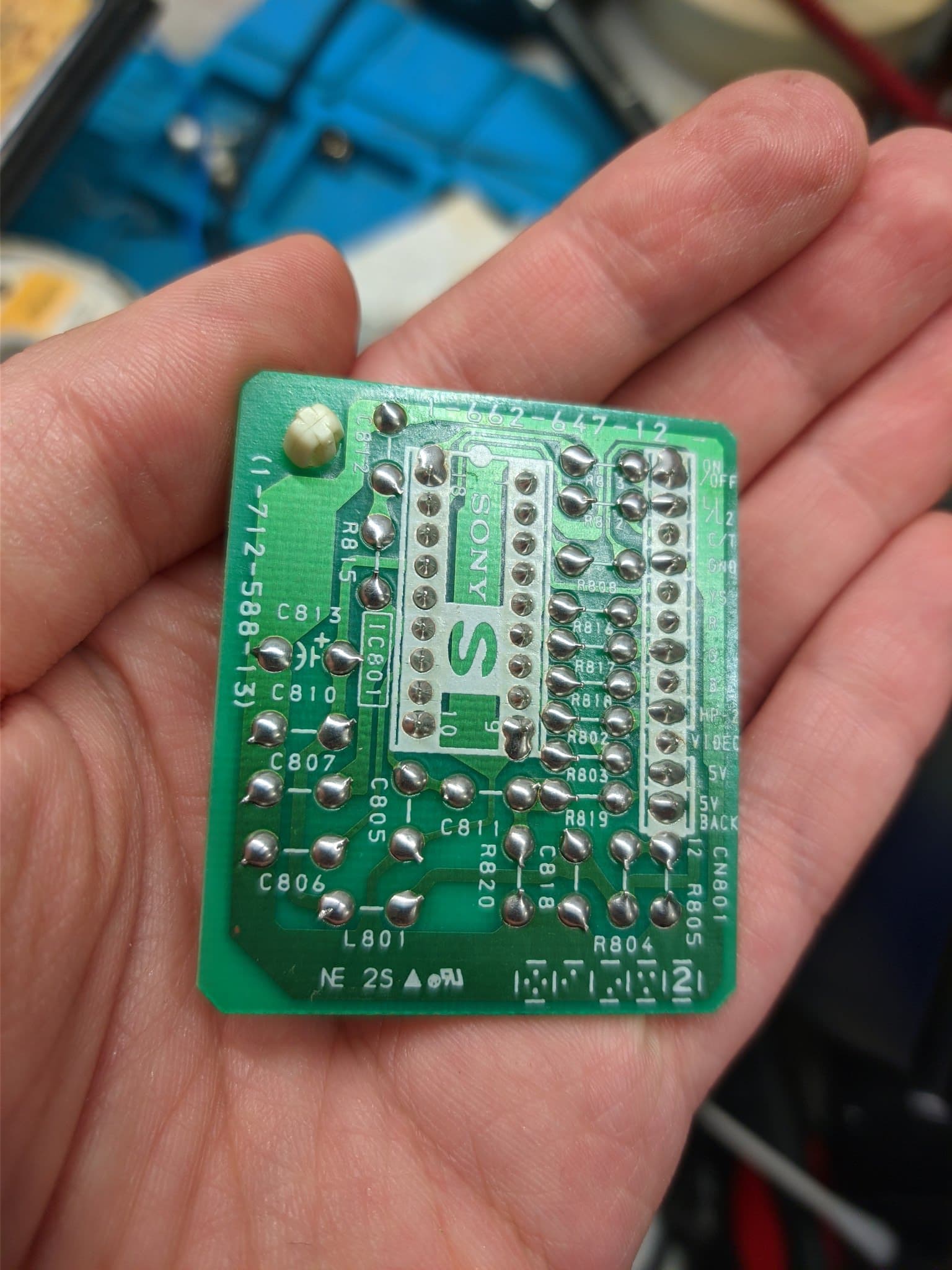 Sony PVM S-board held in hand showing recapped and reflowed capacitors C806-C815, R801-R803, with folded capacitor modification visible.