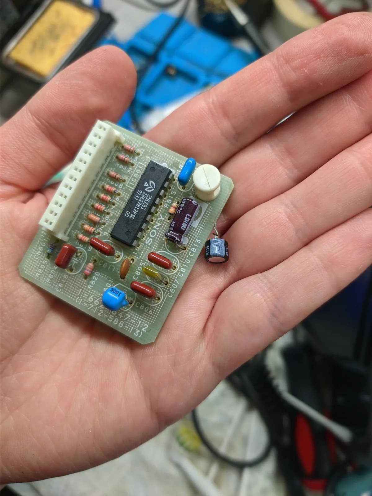 Close-up of recapped S-board from Sony PVM-14M4J showing folded capacitor, IC chip, resistors, and reflow solder joints during maintenance repair.