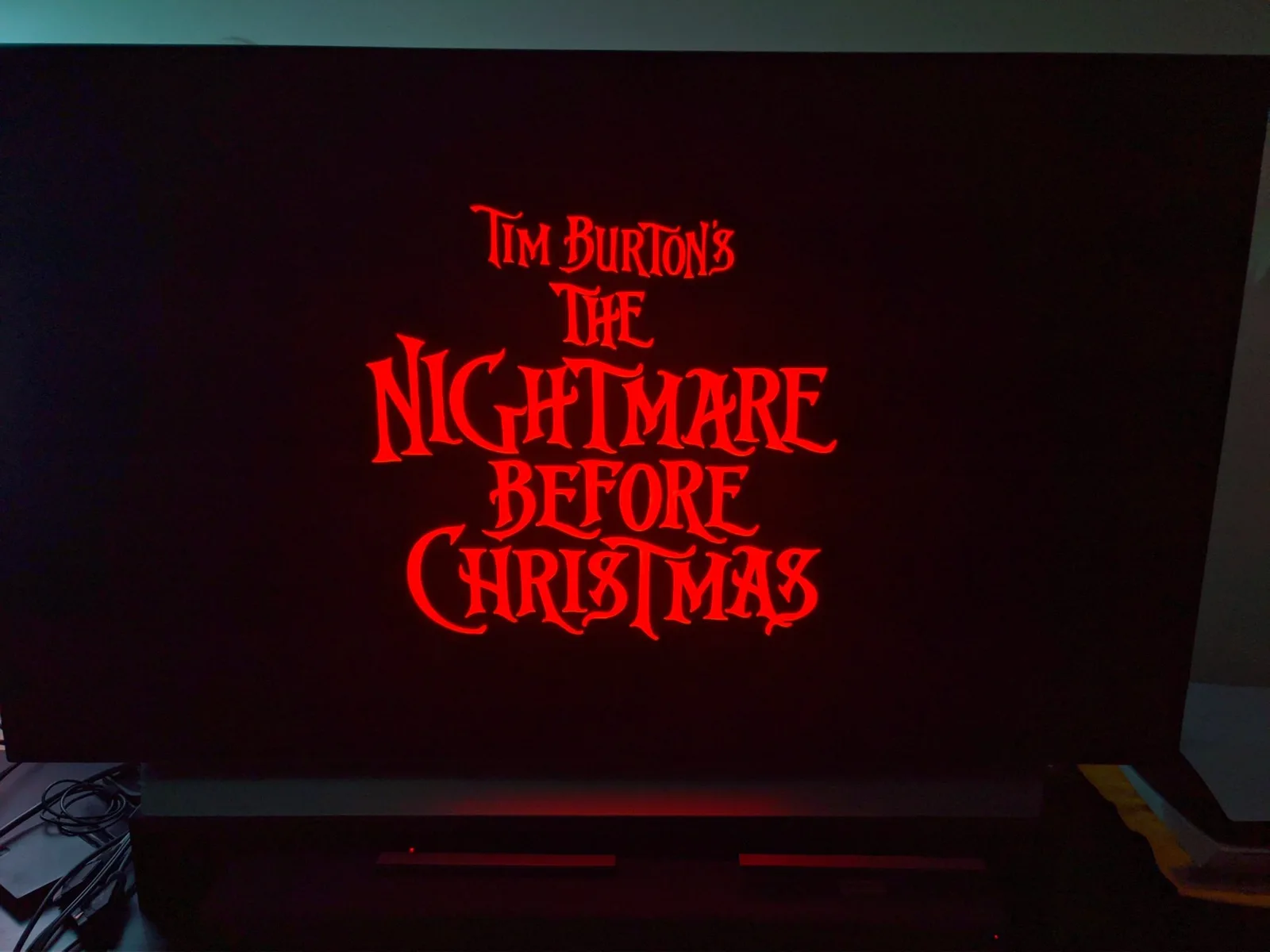 A red title card reading 'Tim Burton's The Nightmare Before Christmas' on a black screen, shown on an LG C1 OLED TV on a media stand in a dark room.