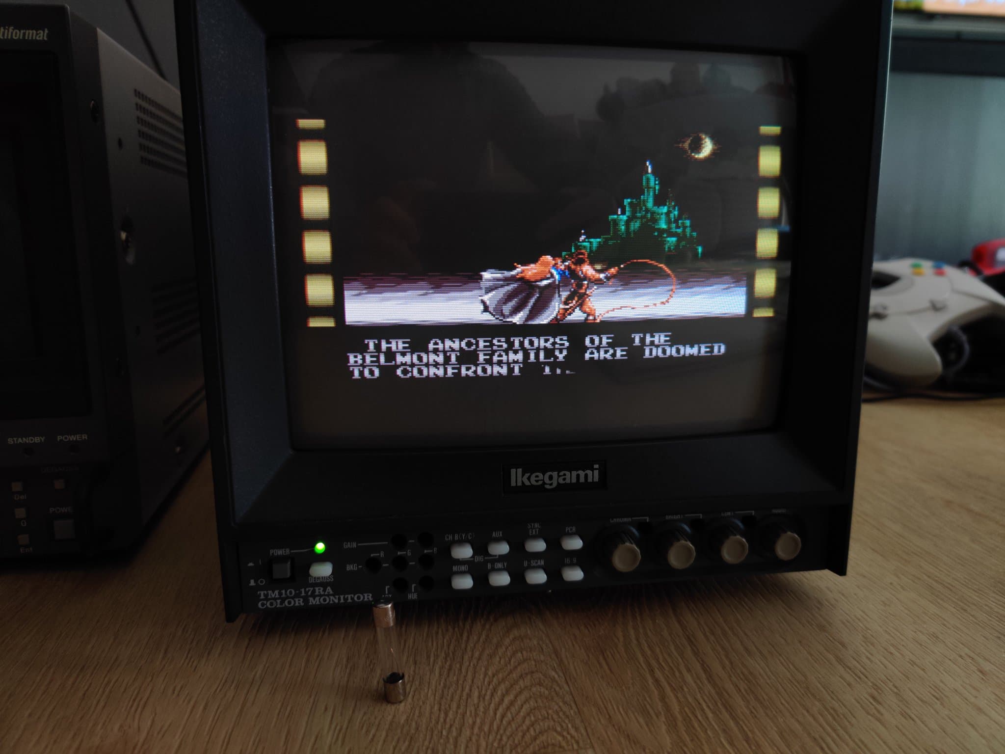 Ikegami TM10-17RA monitor running Vampire Killer (Castlevania: Bloodlines), the intro text about the Belmont family on screen, a glass fuse standing on the desk in front.