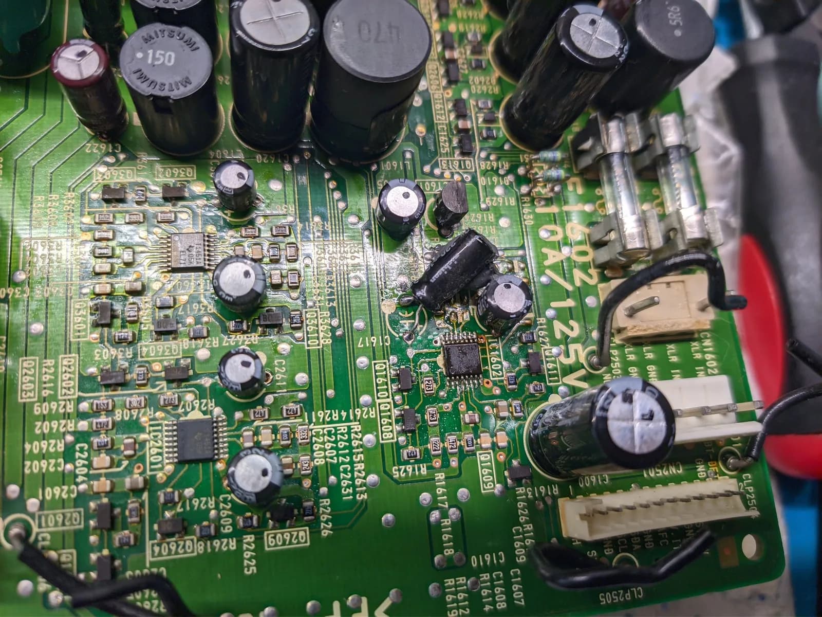 Close-up of the Sony BVM-D9H5J D board (deflection board), component side: a capacitor at the centre of the frame with a blob of solder on one leg, likely a previous servicer's attempt to restore continuity to a compromised pad, a MITSUMI-marked component (not a capacitor, possibly an inductor) nearby, silkscreen designators including C1602 and C1607, and some darkened residue around the components.