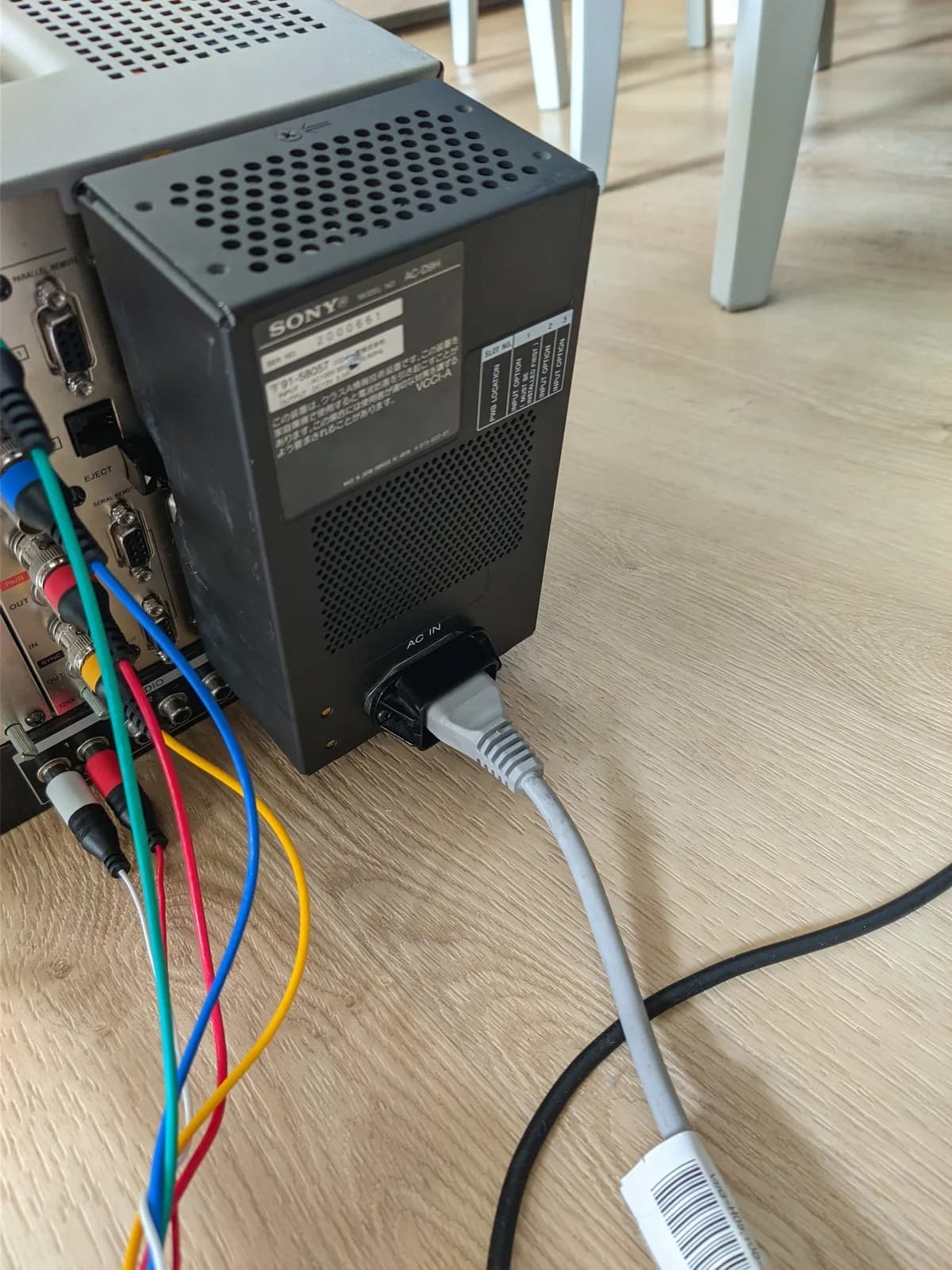The Sony BVM-D9H5J PSU module (black perforated case, SONY nameplate) reinstalled in the partially opened monitor after the recap, colourful internal wires (red, green, blue, yellow) at left and a grey AC power cable connected for testing.