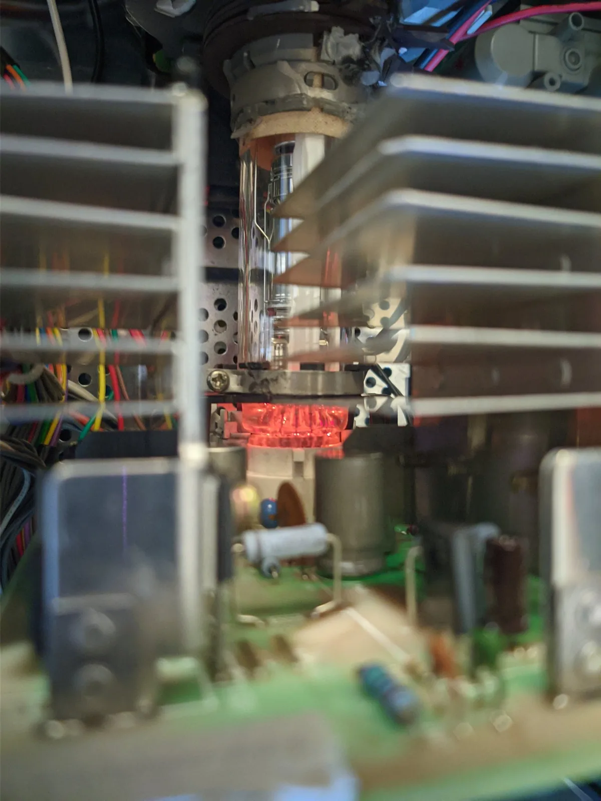 Close-up inside the powered-on Sony BVM-D14H1E, the CRT's heater filament glowing orange-red at the base of the glass tube neck, framed by metal heatsink fins, colorful wiring, and a green circuit board.
