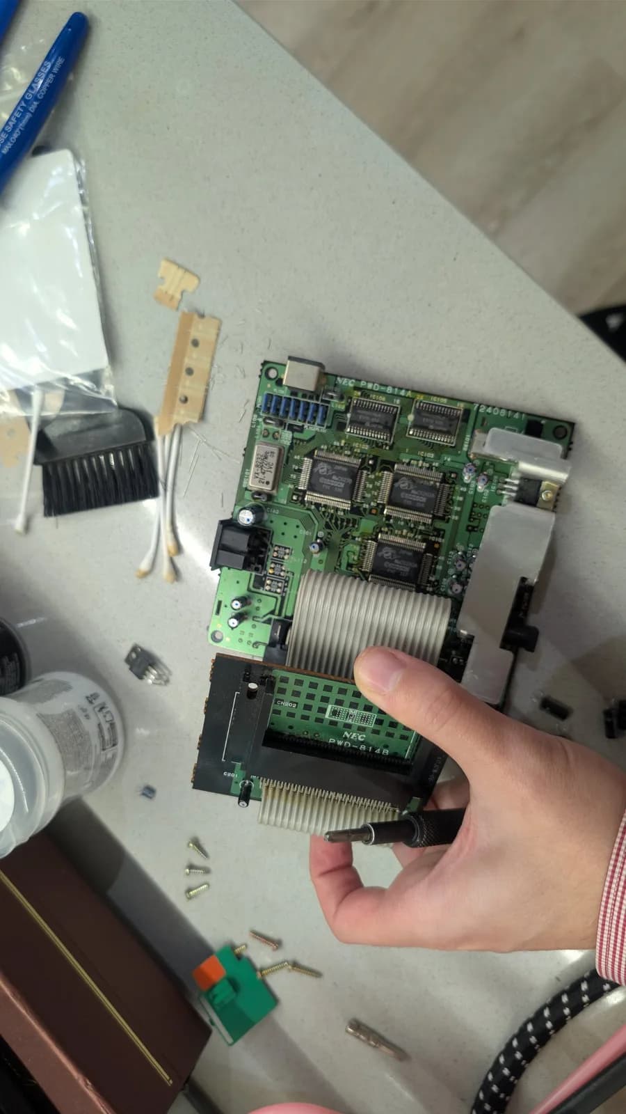 Hand holding the recapped NEC PC Engine CoreGrafx mainboard along with a screwdriver, the new capacitors, voltage regulator and ICs visible.