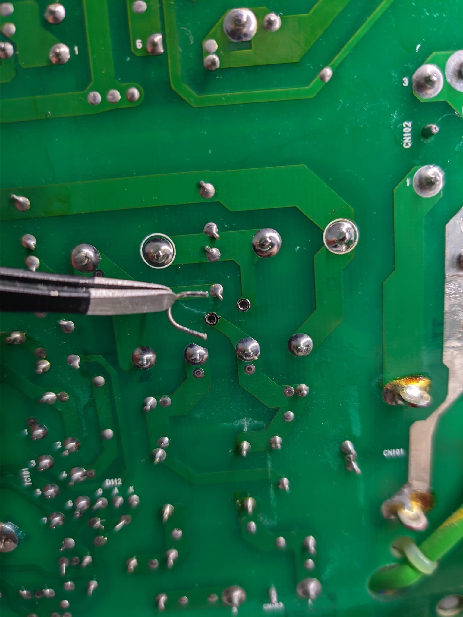 Tweezers removing a soldered wire link from the underside of the Ikegami TM10-17RA power supply board during the voltage conversion.