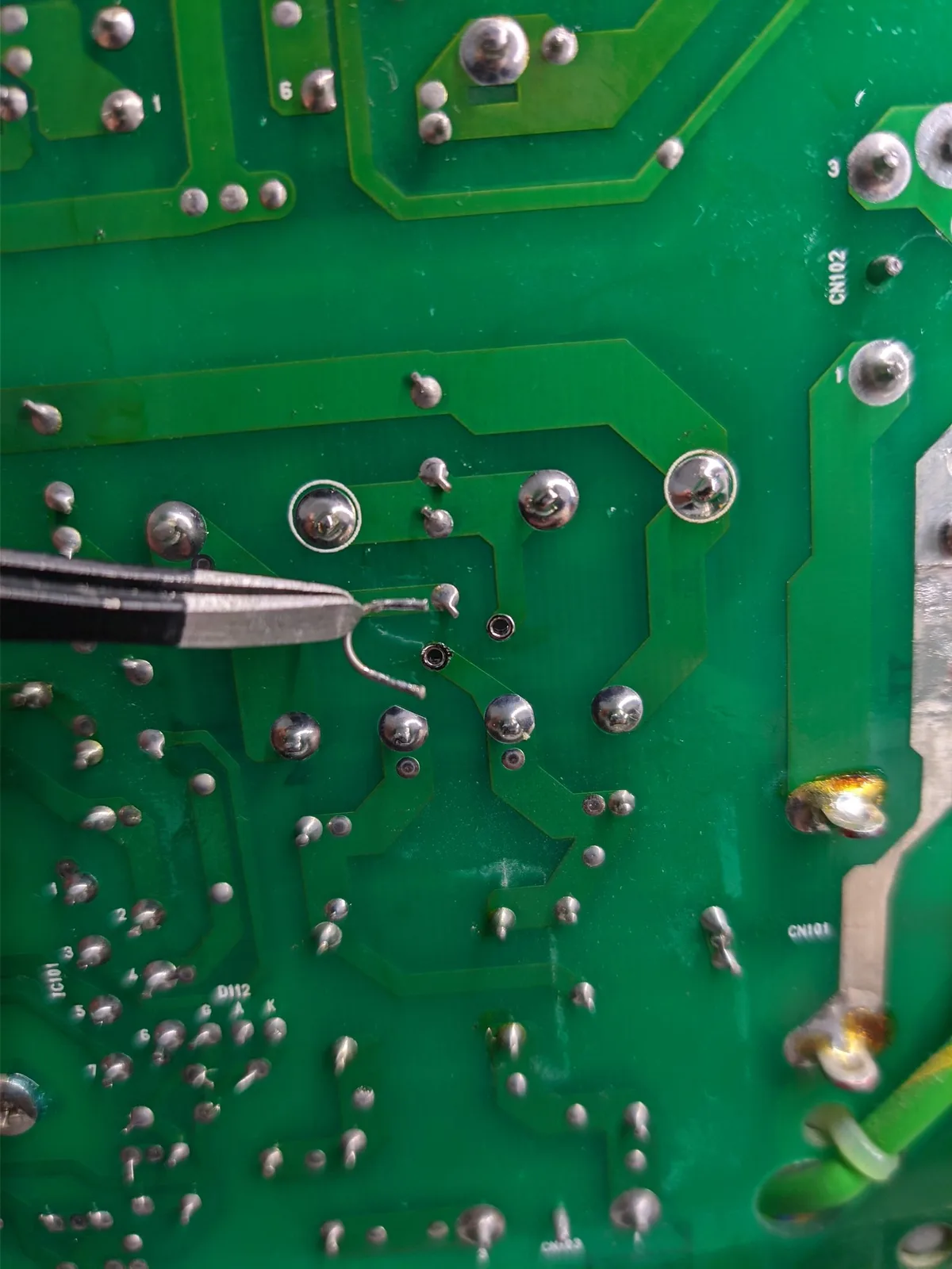 Tweezers removing a soldered wire link from the underside of the Ikegami TM10-17RA power supply board during the voltage conversion.