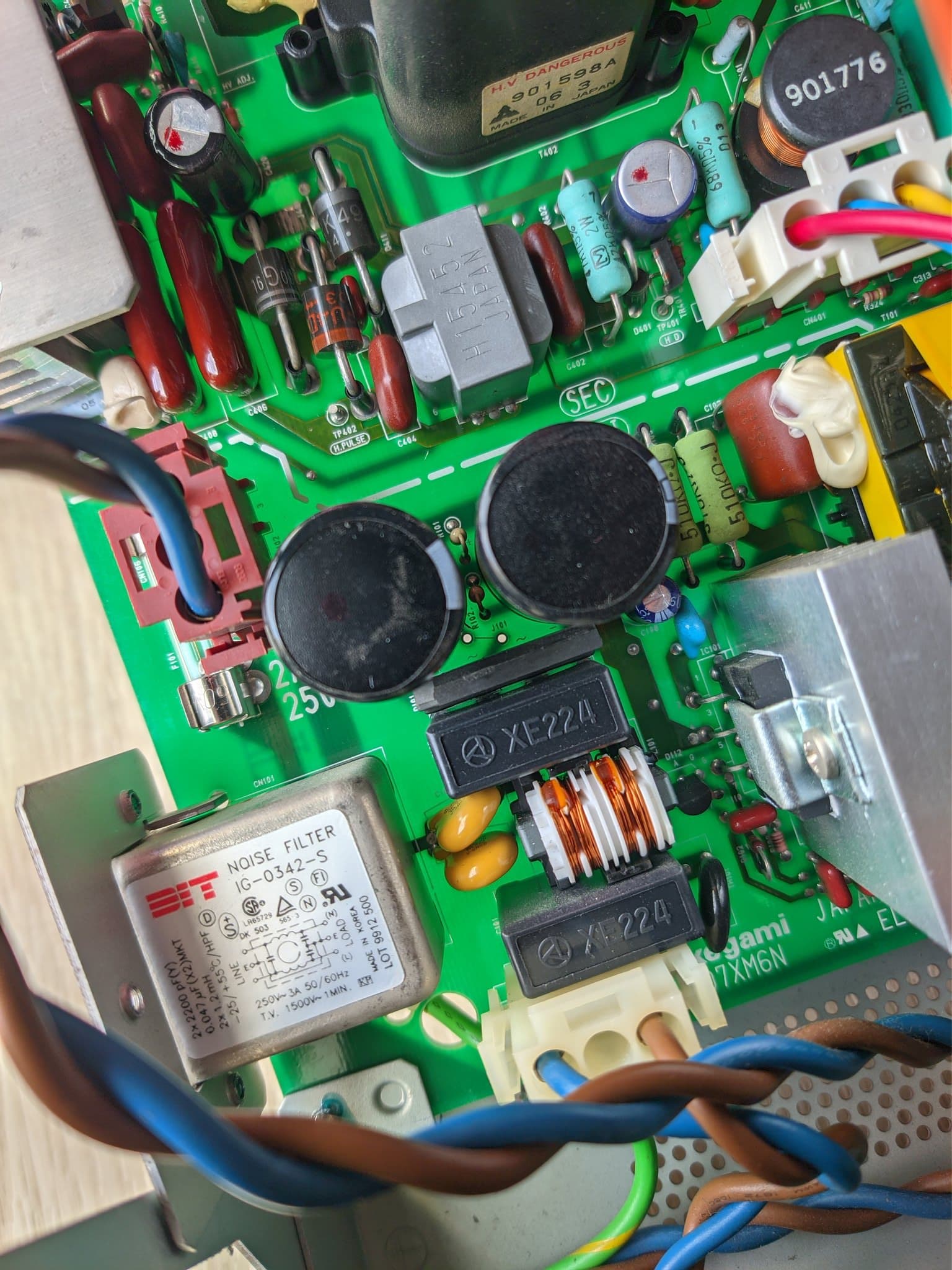 Component side of the Ikegami TM10-17RA power supply board showing the F101 fuse, the two large filter capacitors, and the J101 position with its holes exposed where the jumper link was removed for 200-240V.
