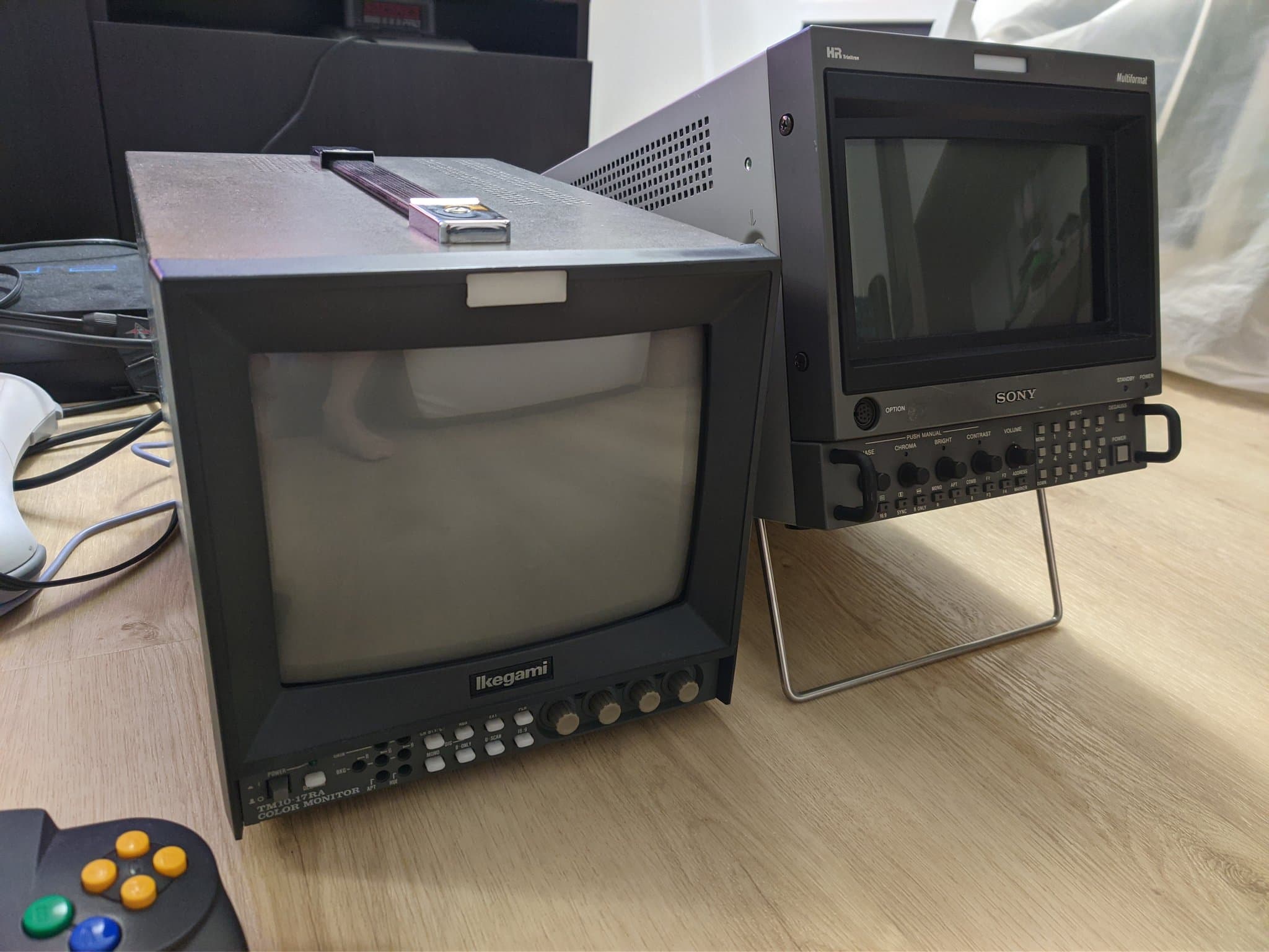 Two broadcast CRTs side by side with blank grey screens: the Ikegami TM10-17RA (left, shadow mask) and a Sony BVM-D9H5J (right, aperture-grille Trinitron), a controller in front.