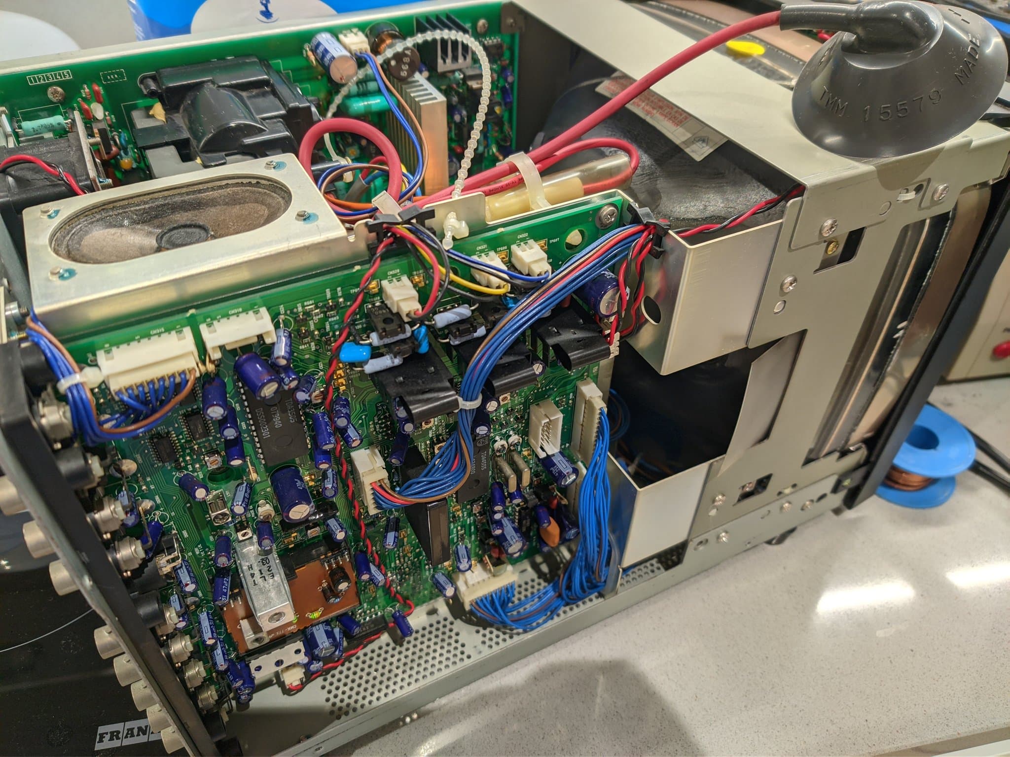 Open Ikegami TM10-17RA interior during a cleaning and service pass: the main PCB with blue capacitors, a speaker, red and blue wiring harnesses, and the CRT and transformer chassis.