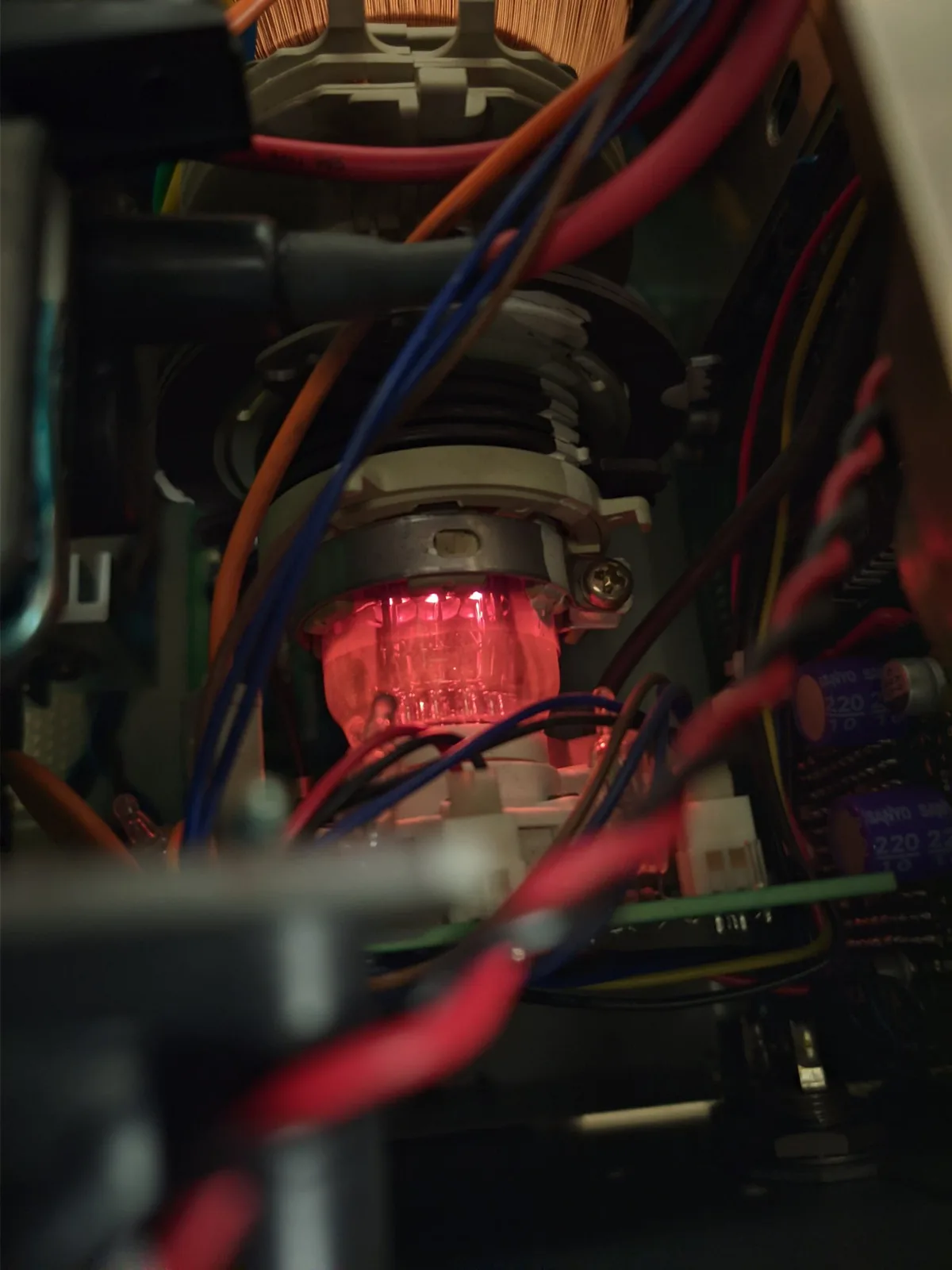 The Ikegami TM10-17RA powered on and running, its CRT electron gun glowing red-orange inside the tube neck behind the deflection yoke, amid the multicoloured chassis wiring.